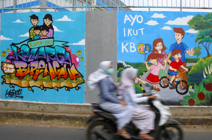 Warga melintasi mural Kampung KB di Jalan Armed VII, Kelurahan Cikiwul, Bekasi, Jawa Barat.