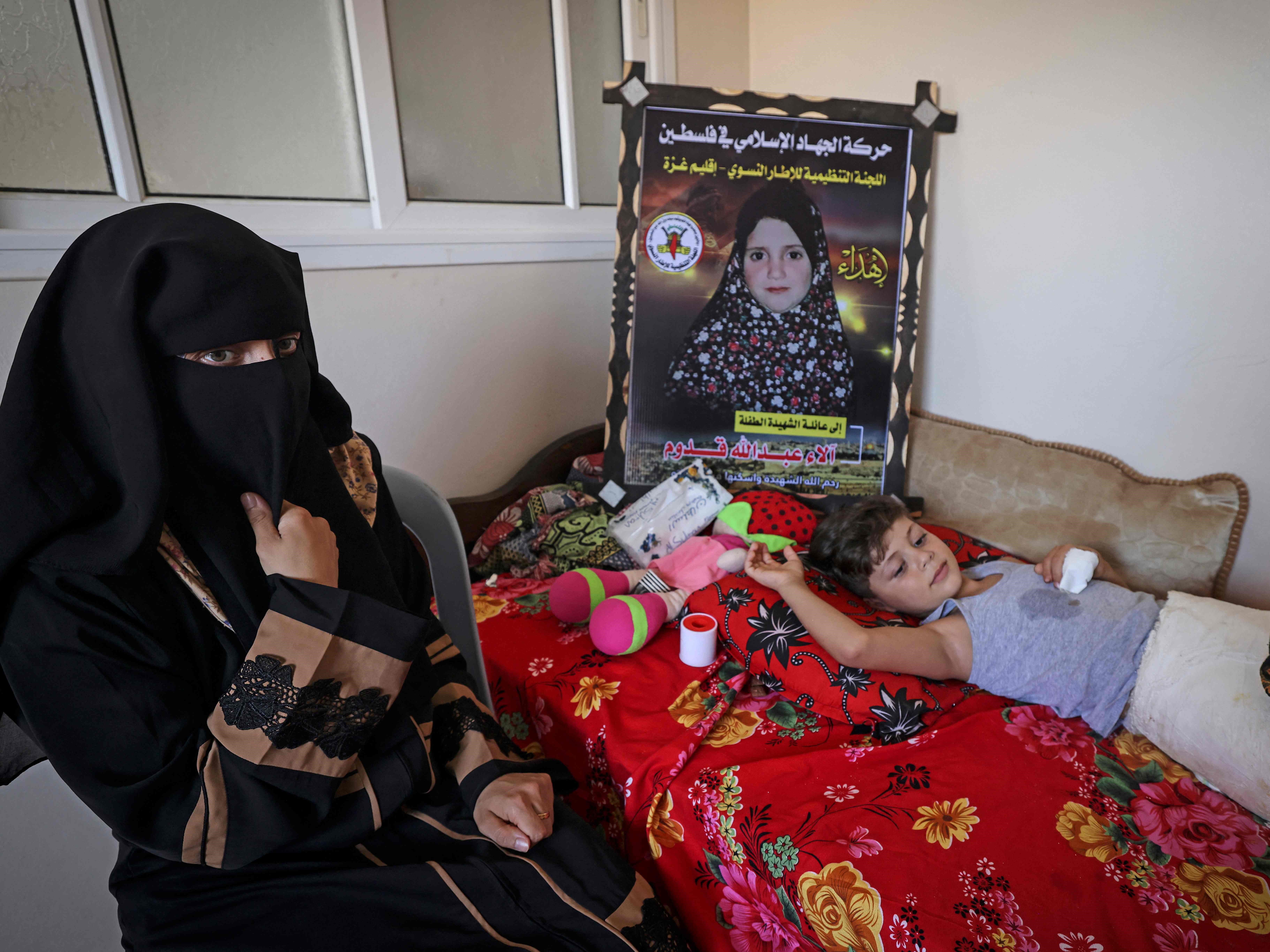 Rasha Qadoom duduk di samping anaknya yang terluka, Rayed, di dekat foto putrinya yang berusia lima tahun, Alaa, yang tewas..
