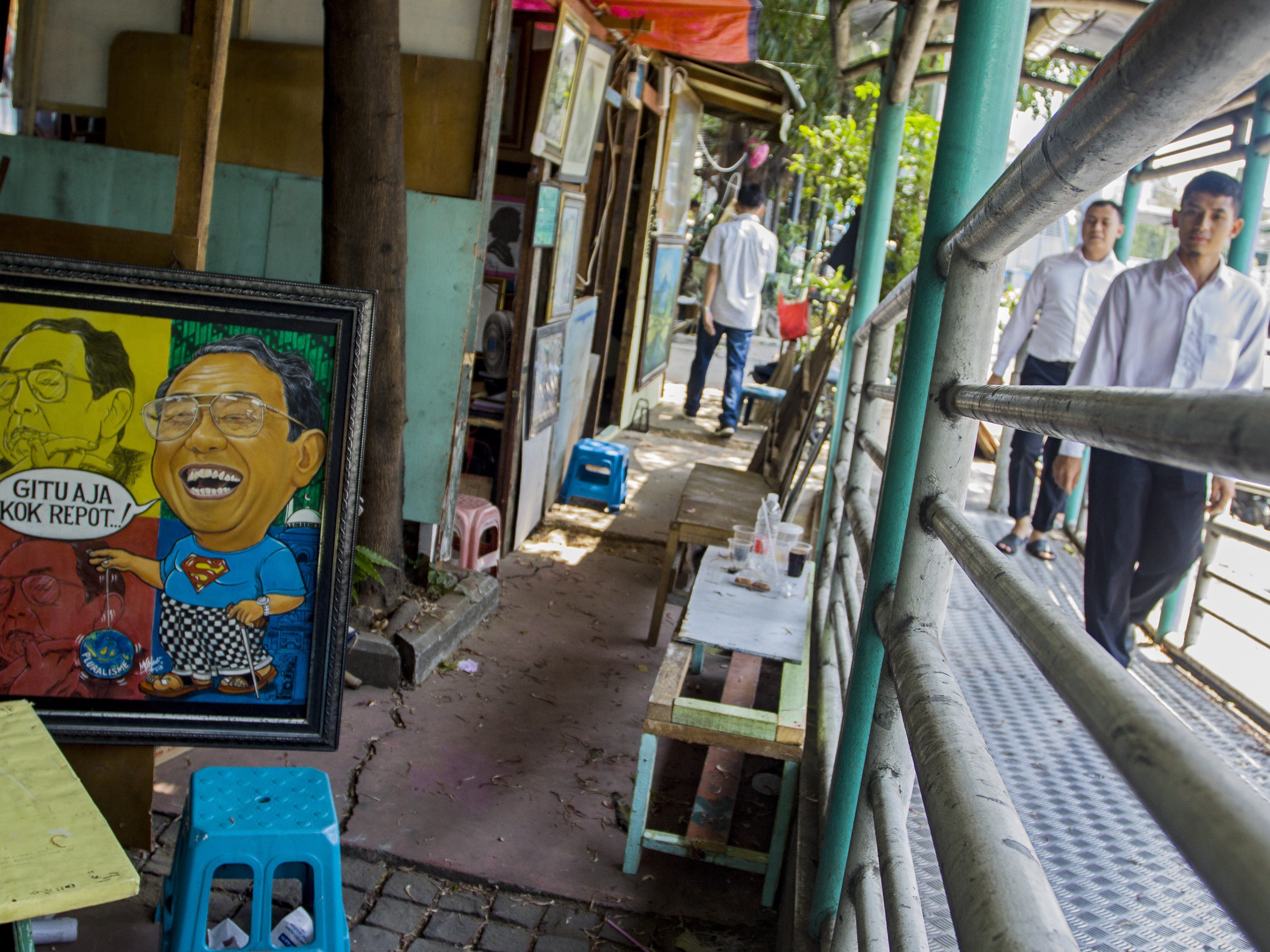 Warga melintas di samping lapak pelukis di Jalan Gedung Kesenian, Pasar Baru, Jakarta.