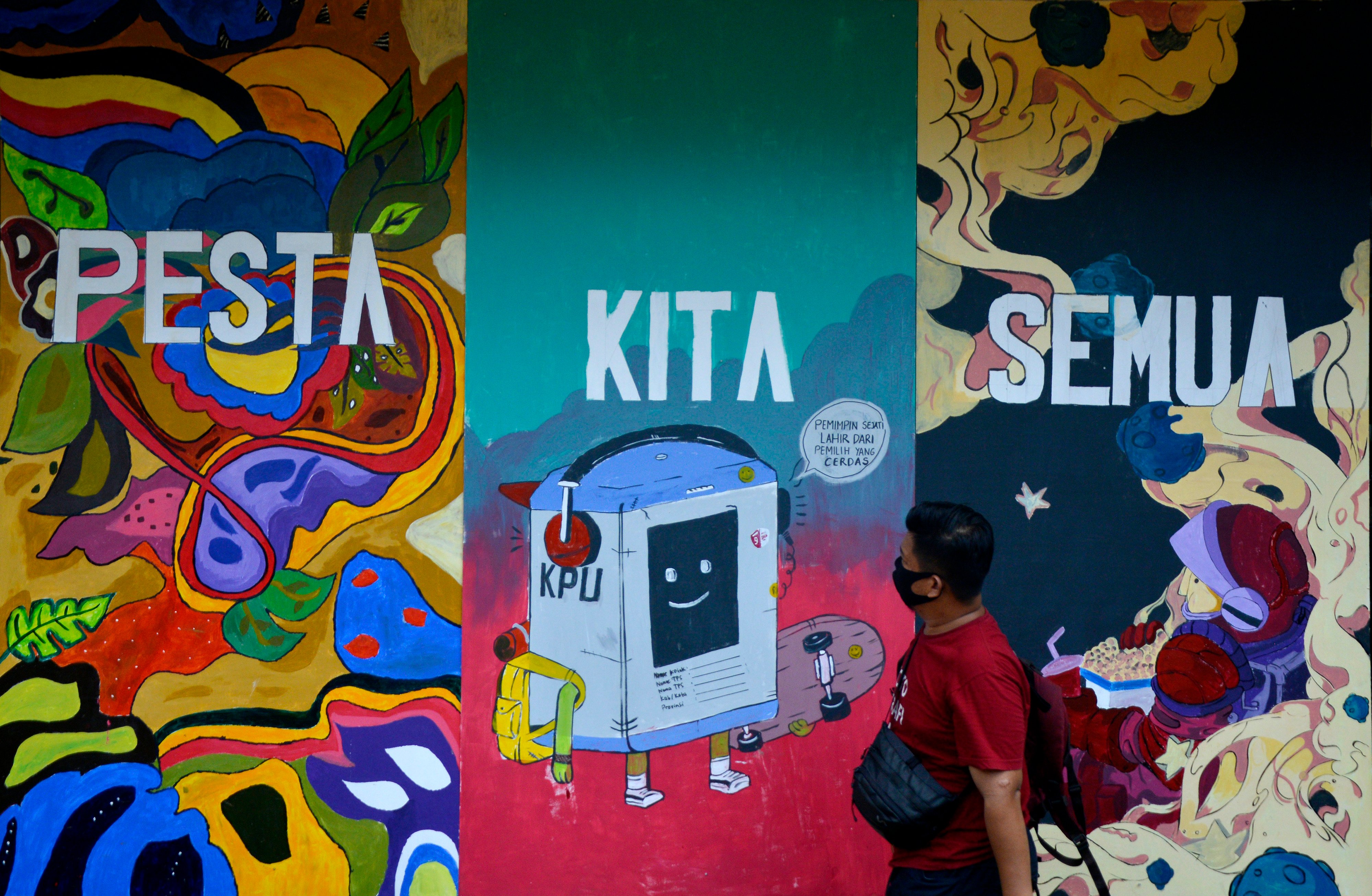 Warga melintas di dekat tembok yang dihiasi mural terkait pemilu.