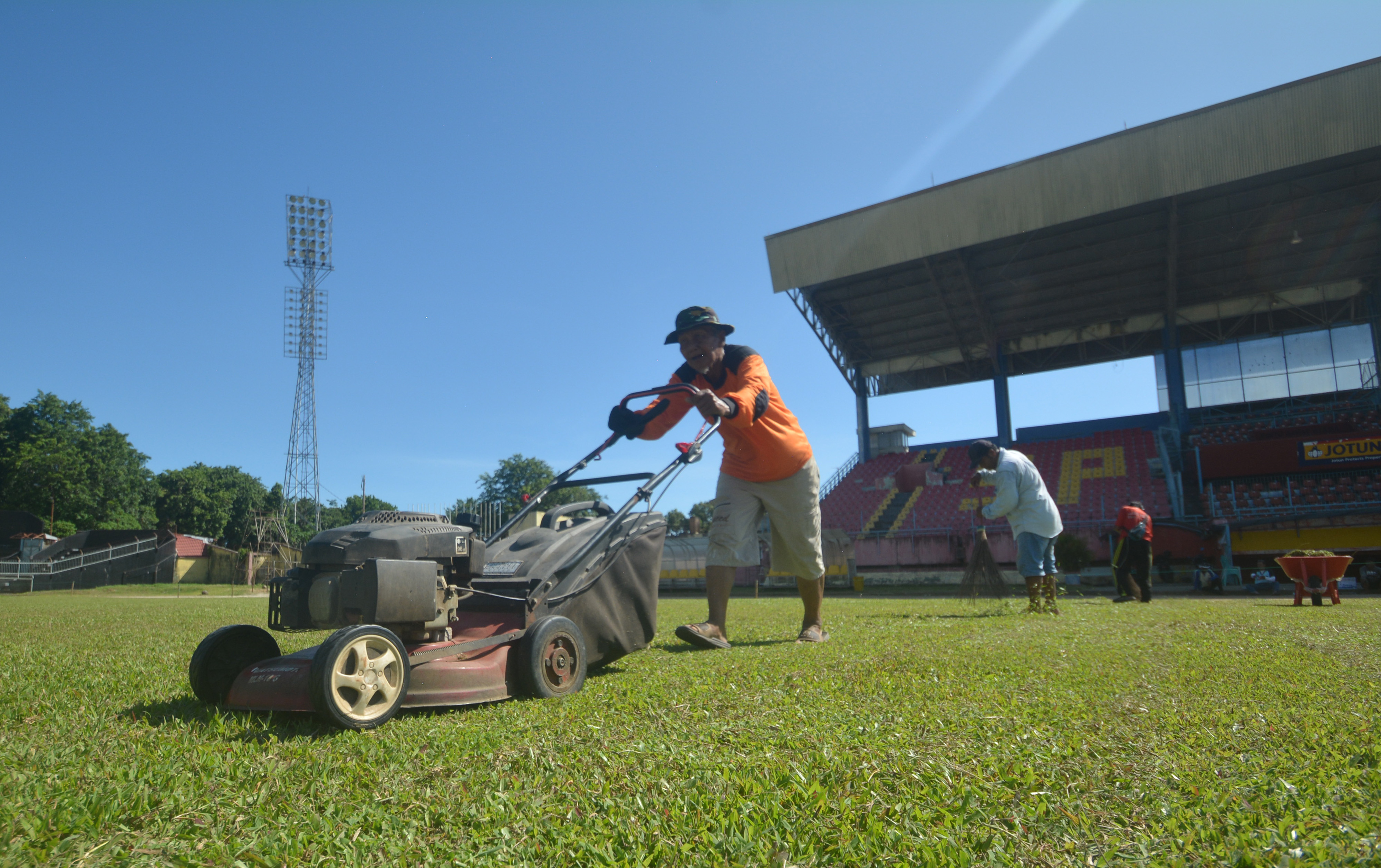 Potret pekerja merawat rumput di lapangan bola.