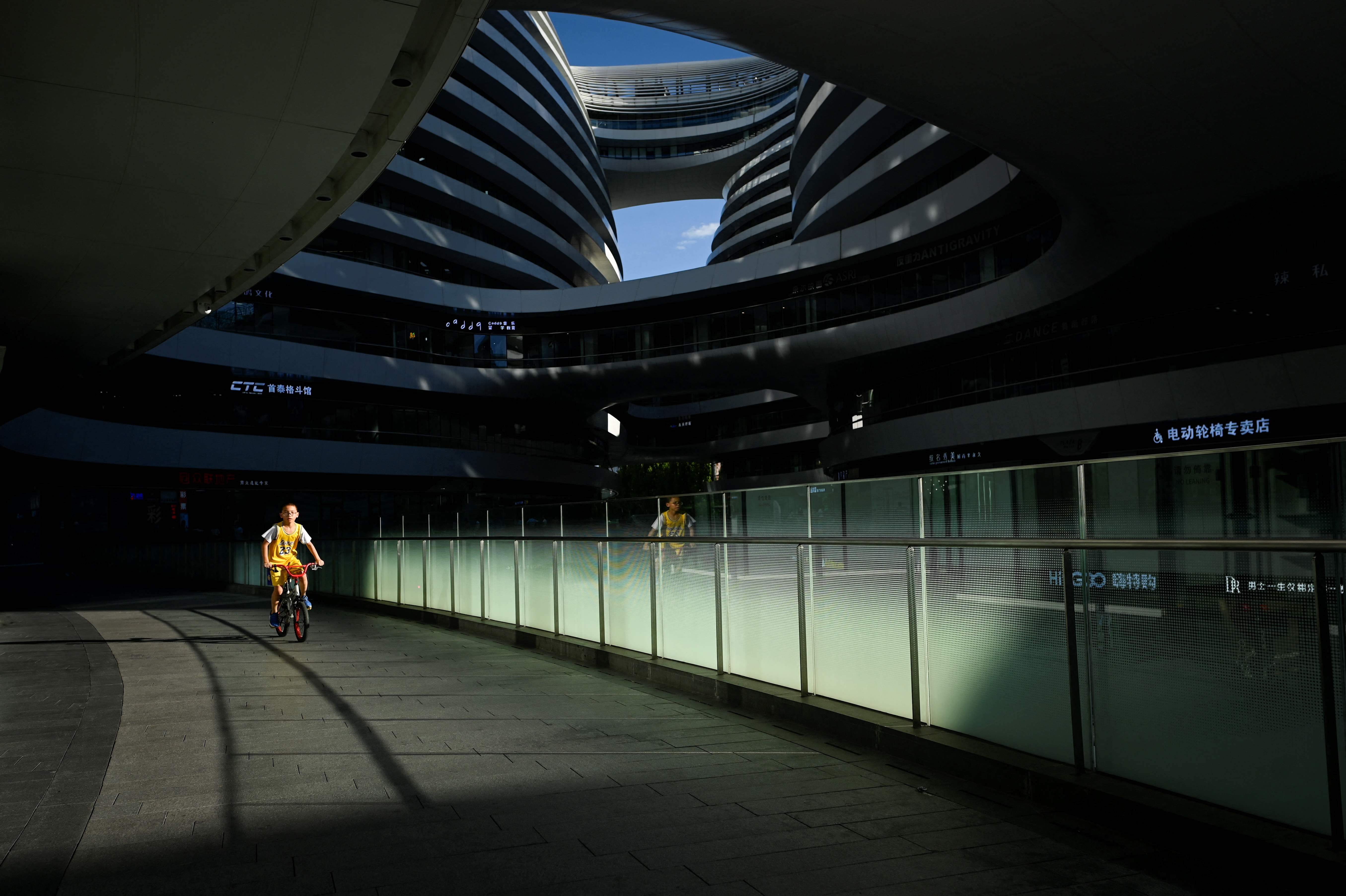 Seorang anak mengendarai sepeda melewati sebuah bangunan kompleks di Beijing yang kosong, Senin (15/8/2022)