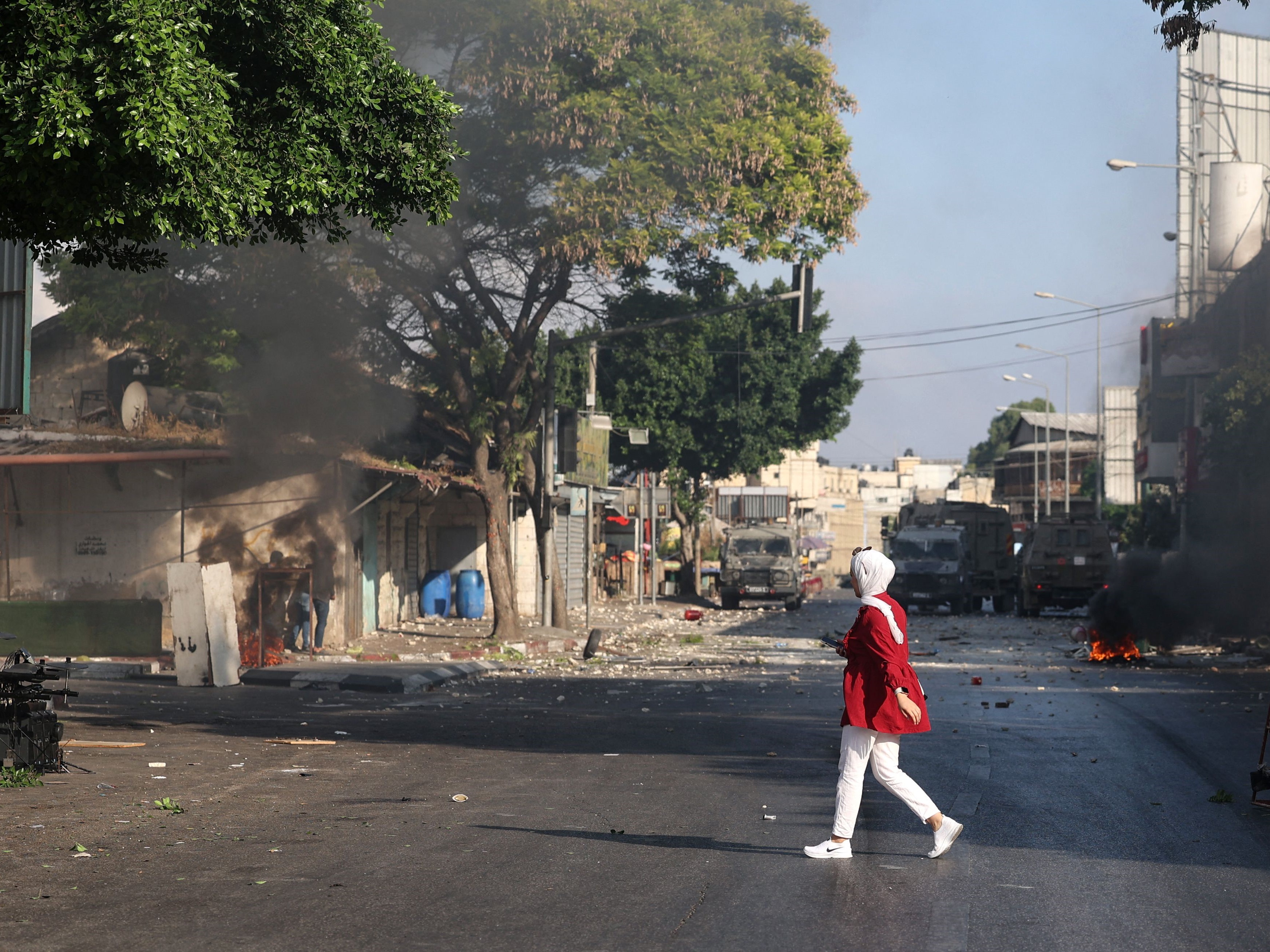 Seorang wanita Palestina berjalan di seberang jalan saat para pemuda bentrok dengan pasukan Israel di kota Nablus, Tepi Barat.
