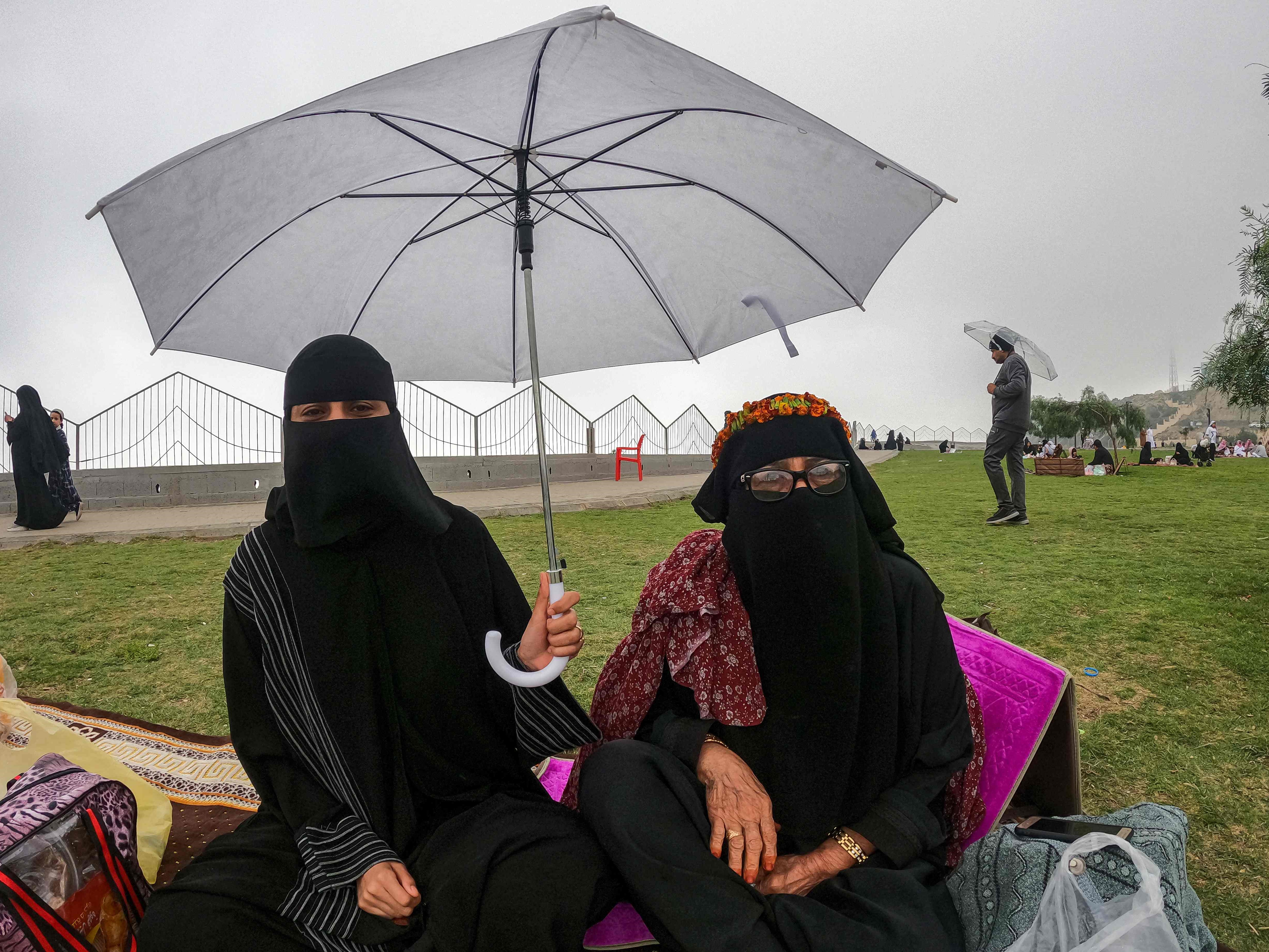 Seorang wanita memegang payung saat dia duduk dengan yang lain di sepanjang tanjung di al-Namas, Provinsi Asir, Arab Saudi.