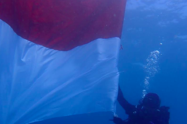 Penyelam memegang bagian Bendera Merah Putih yang dikibarkan di dalam perairan Taman Laut Pandanan.