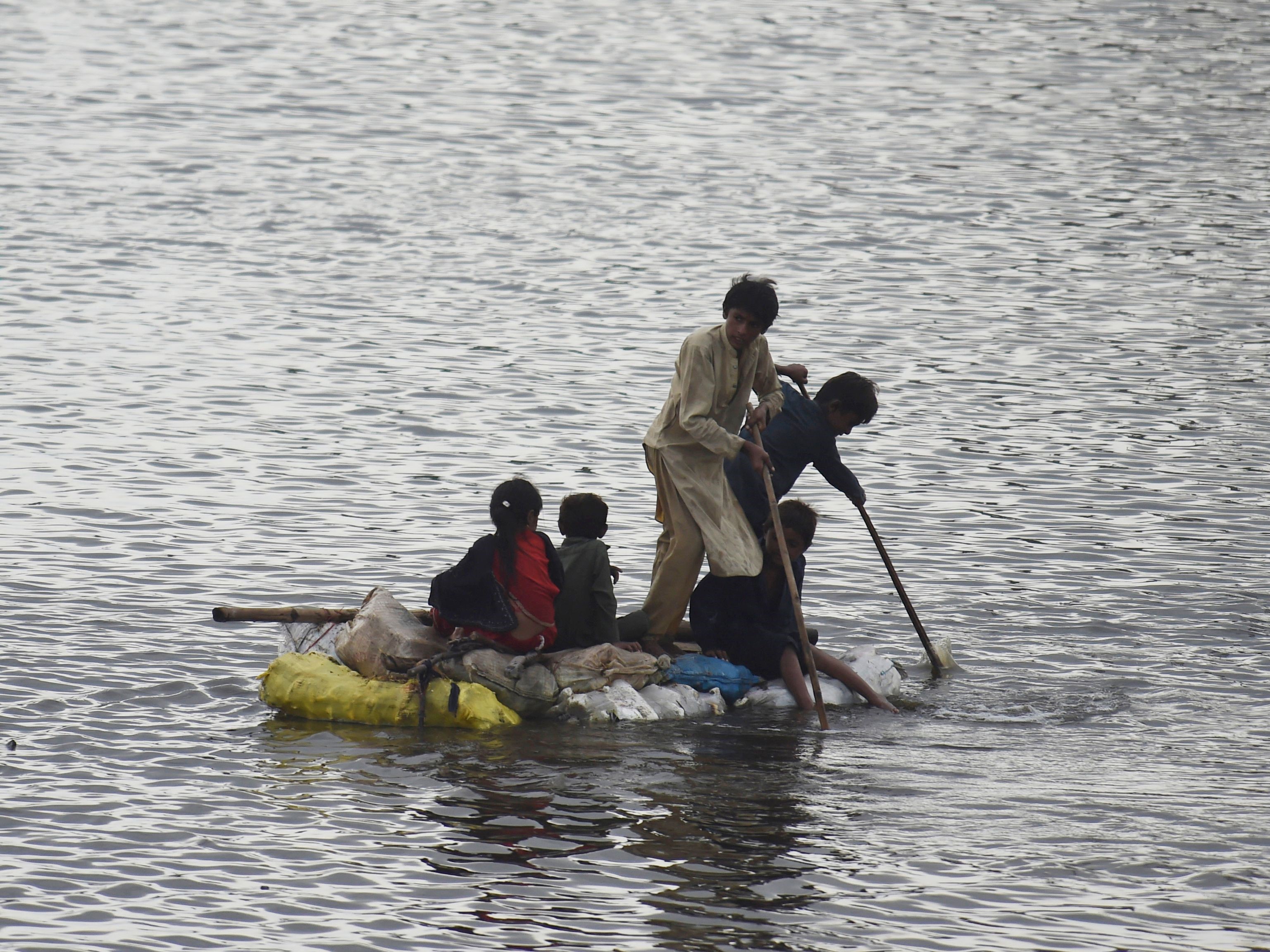 Anak-anak menggunakan rakit untuk berjalan di daerah banjir setelah hujan muson lebat di pinggiran Sukkur, provinsi Sindh, Sabtu (27/8).
