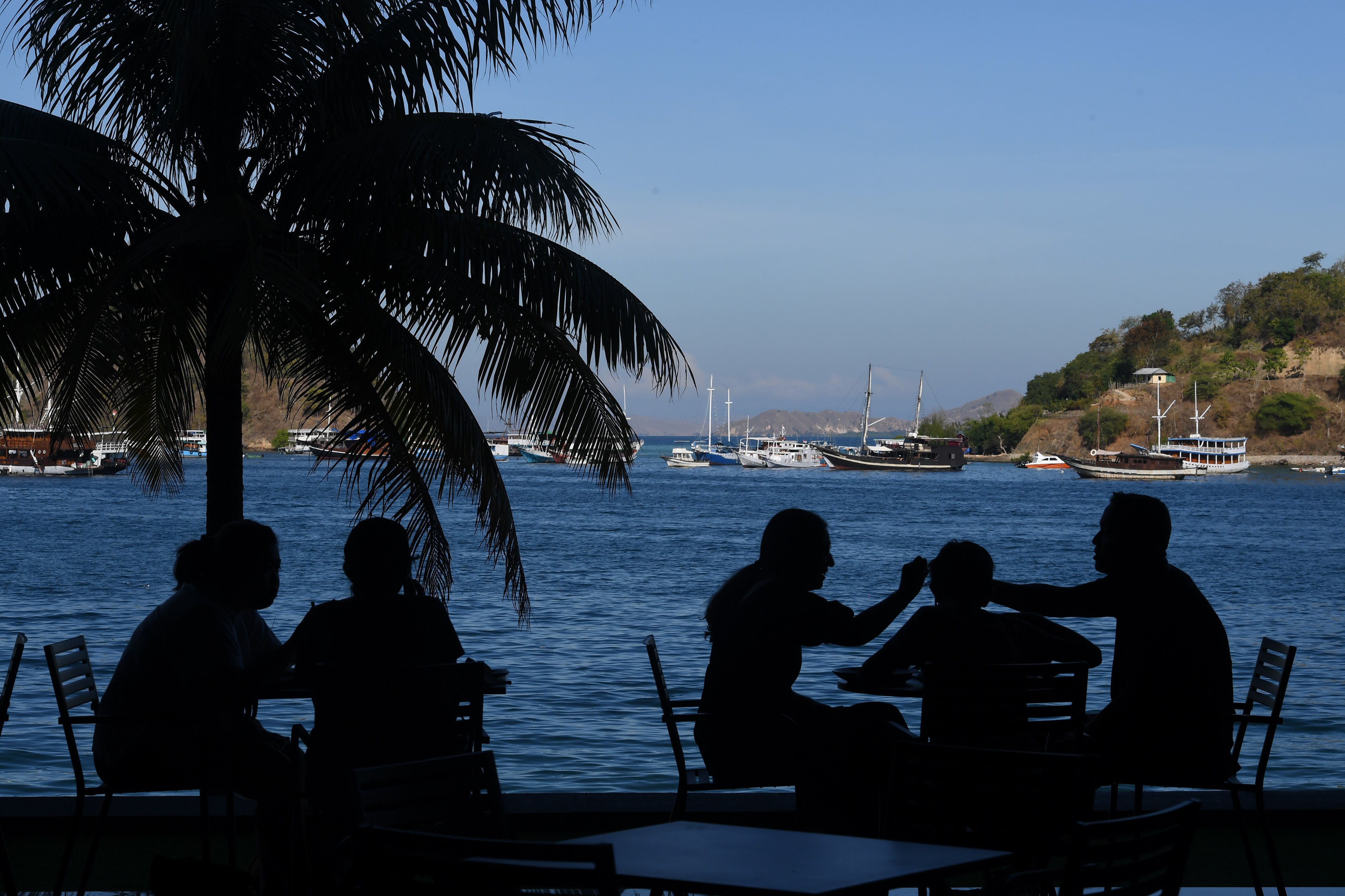 Siluet wisatawan mancanegara menikmati santapan dengan pemandangan perairan Labuan Bajo di Kabupaten Manggarai Barat, NTT.