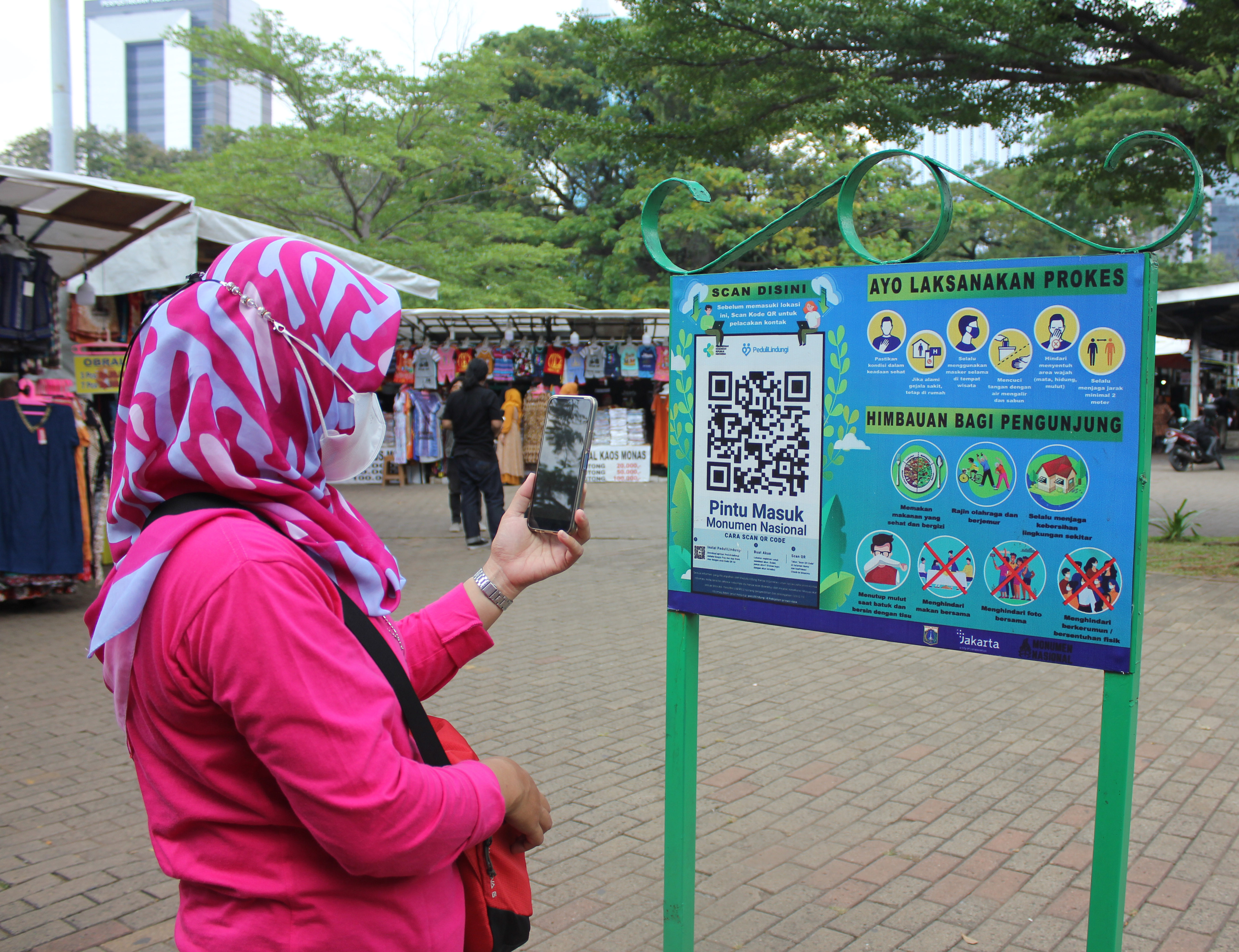 Seorang pengunjung memindai kode batang melalui aplikasi PeduliLindungi sebelum memasuki kawasan Monas di Jakarta.