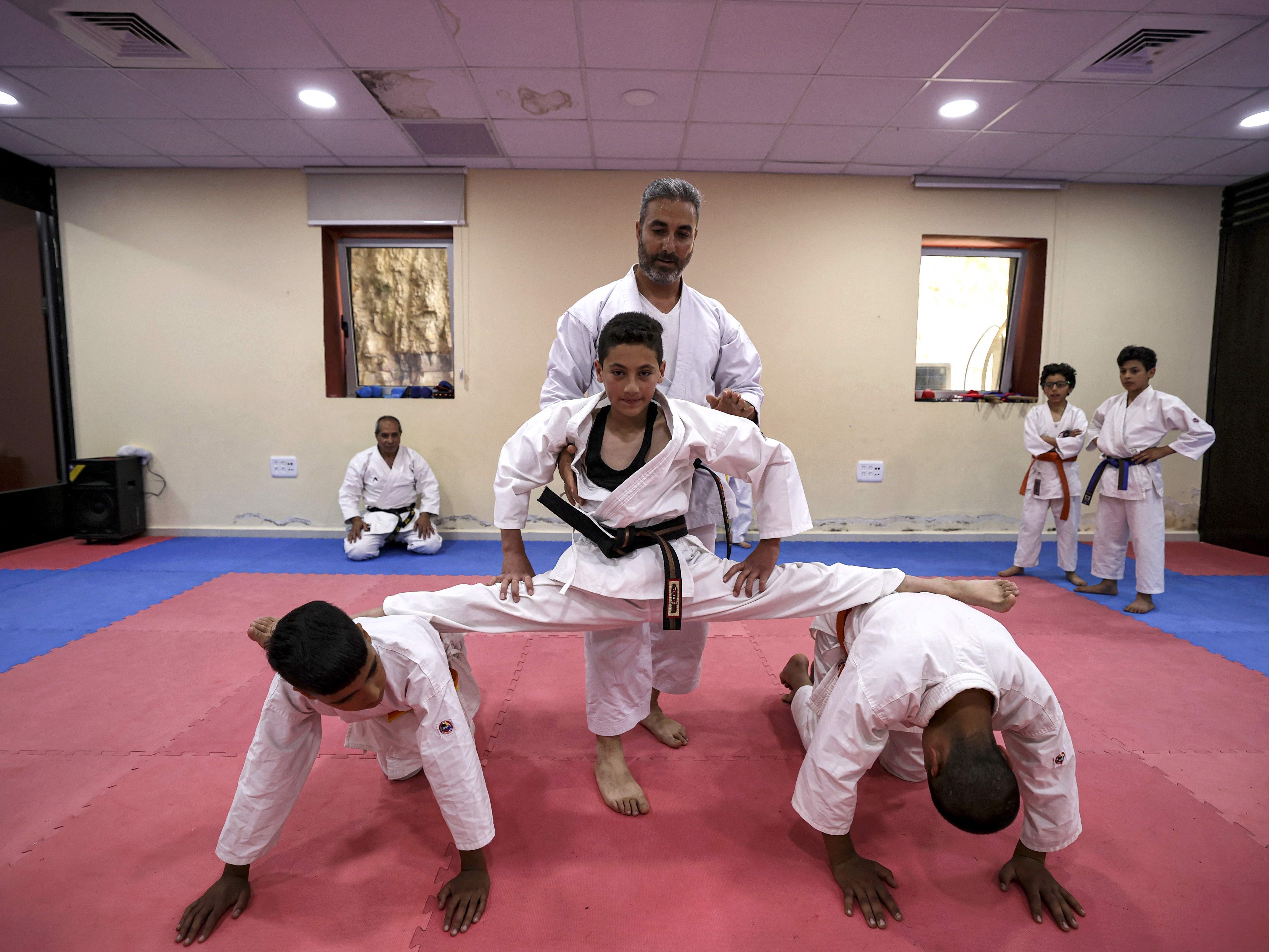Seorang instruktur karate membantu seorang siswa melakukan split di atas dua siswa lain.