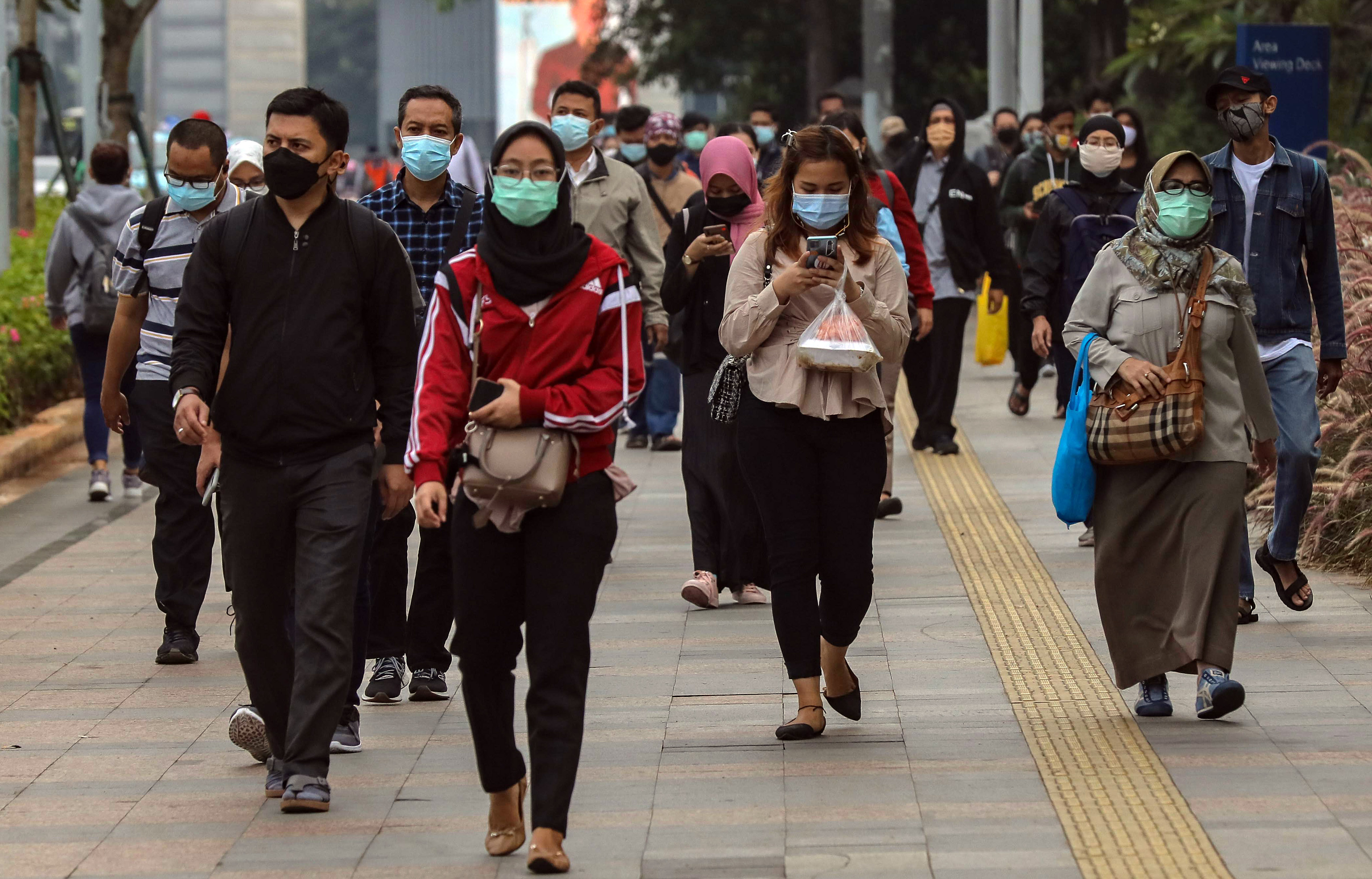 Potret pekerja berjalan di trotoar kawasan Jalan Sudirman, Jakarta.