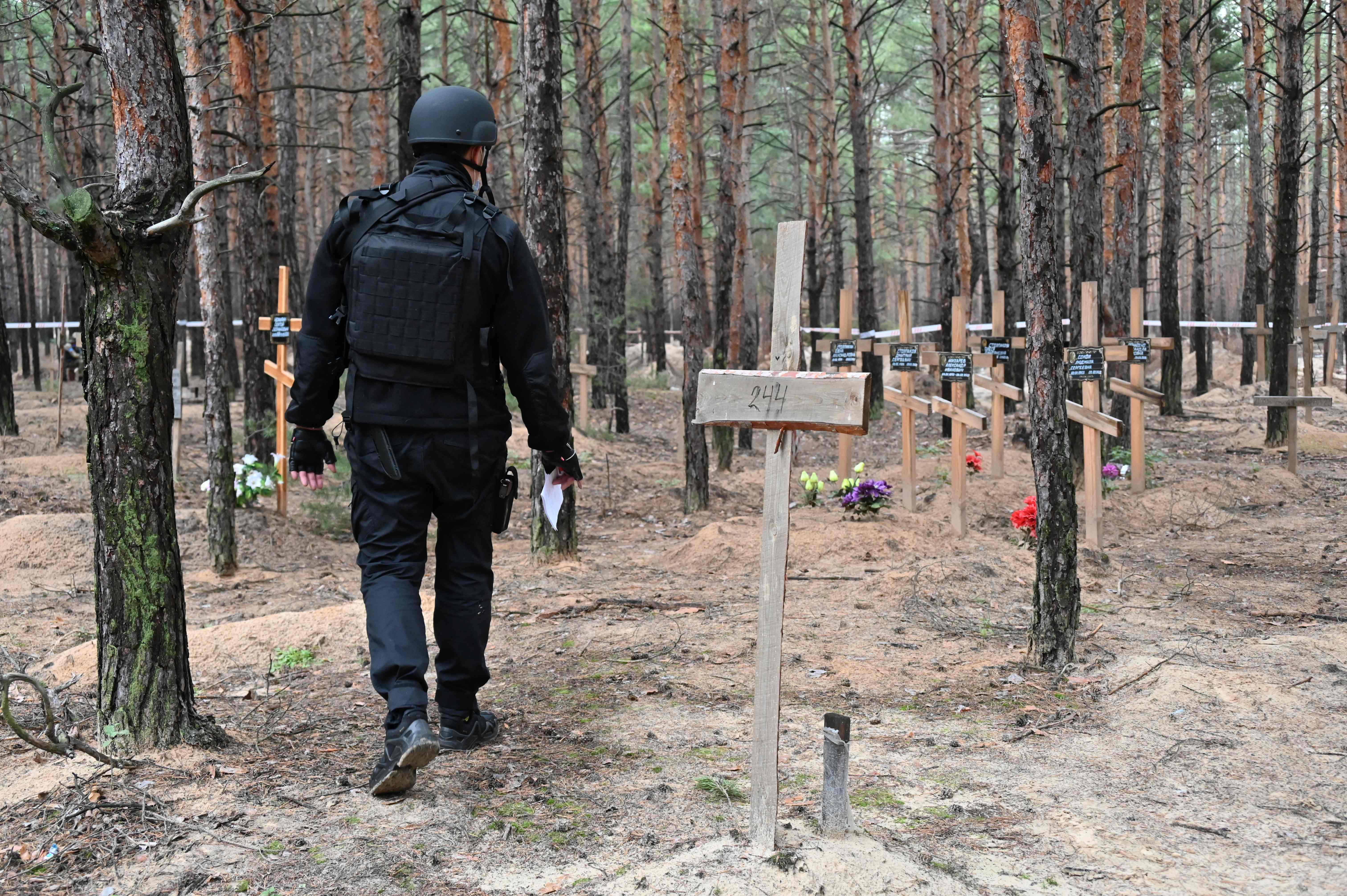 Polisi Ukraina berjalan diantara pemakaman massal di wilayah Lyzum, Ukraina Timur.