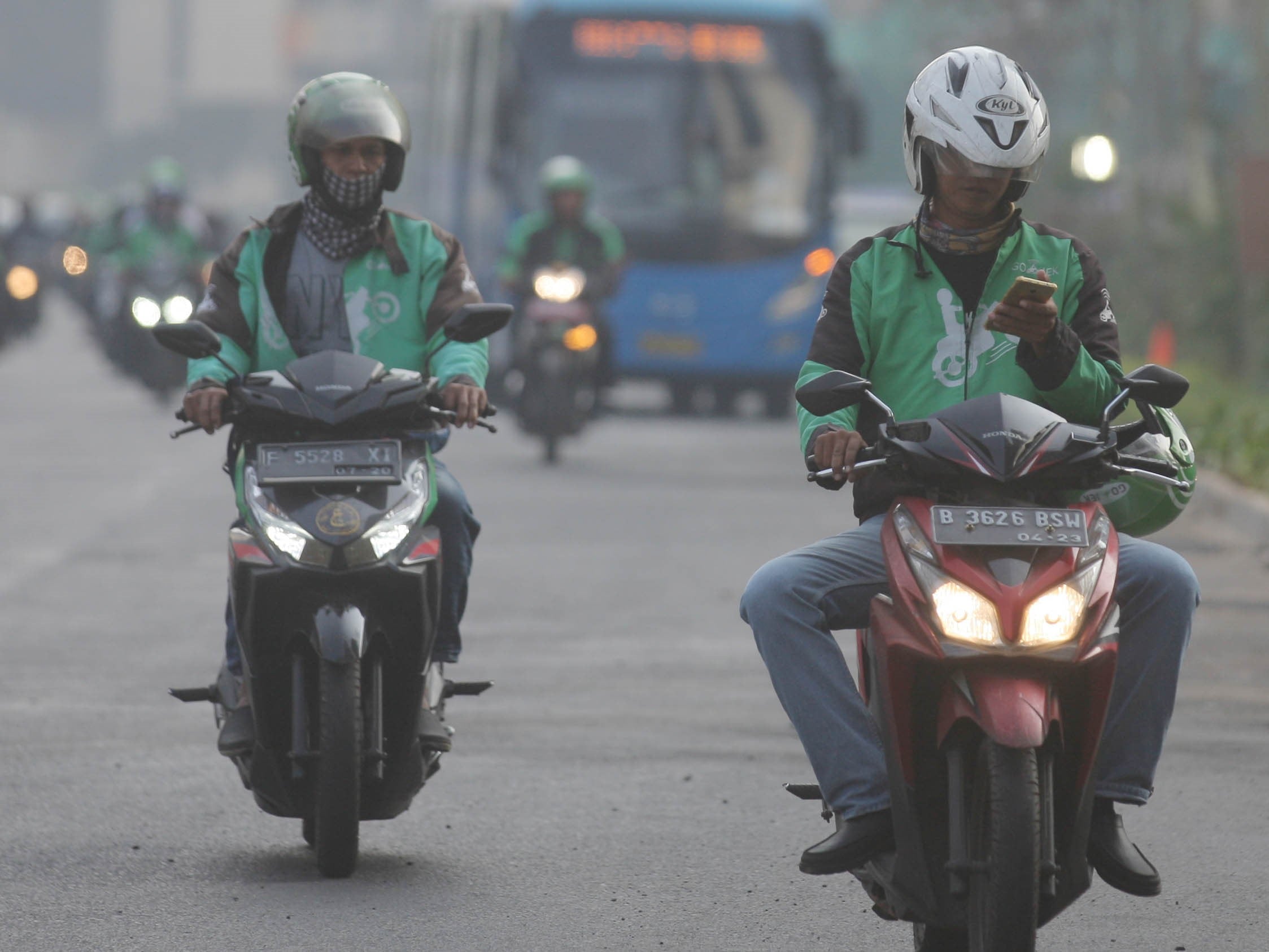 Pengendara sepeda motor ojek online menggunakan telepon pintar saat berkendara di Jalan Sudirman, Jakarta.