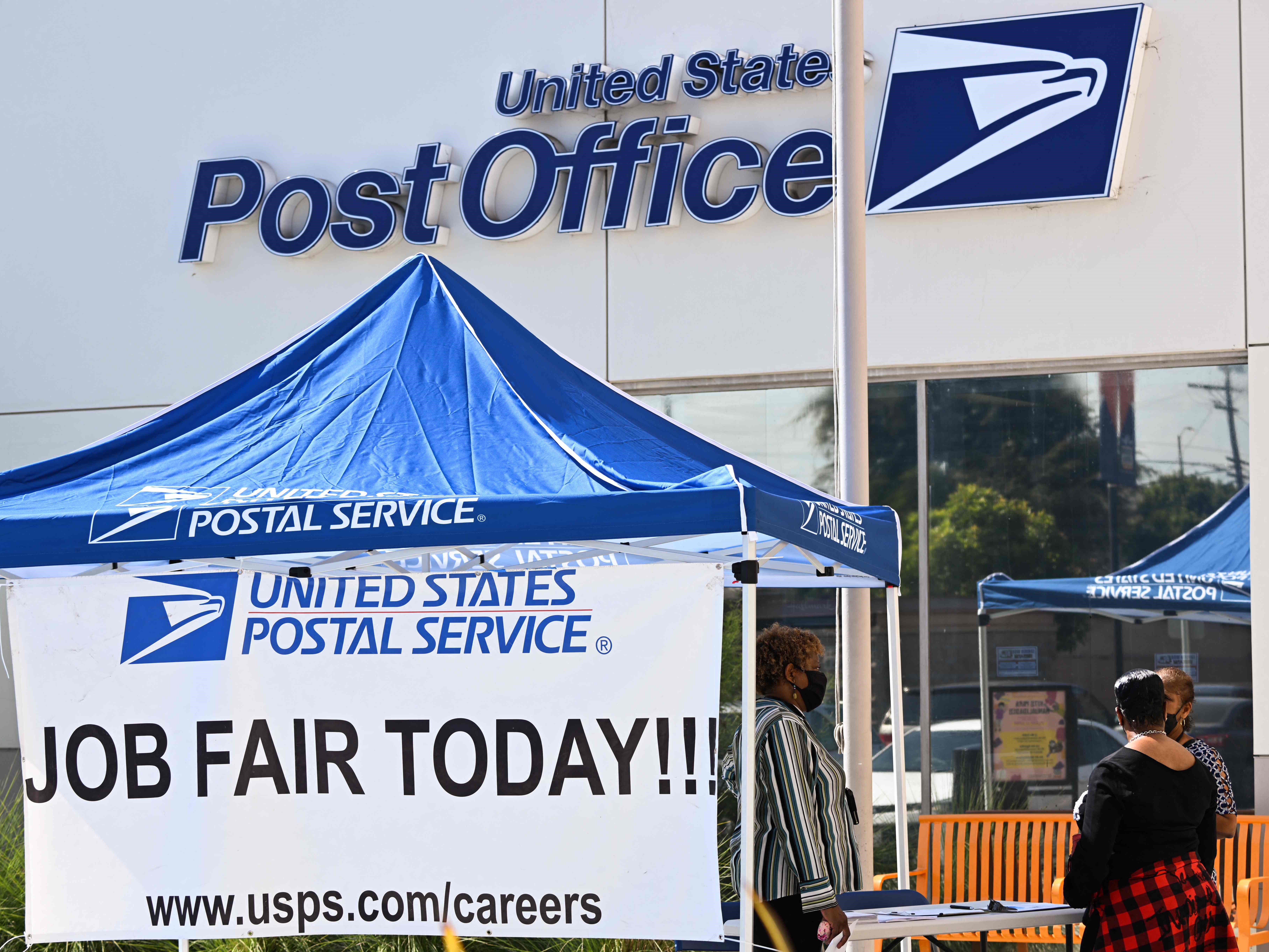 Seseorang menerima informasi pekerjaan selama pameran pekerjaan yang mempekerjakan pekerja dan asisten pembawa surat di kantor pos. 