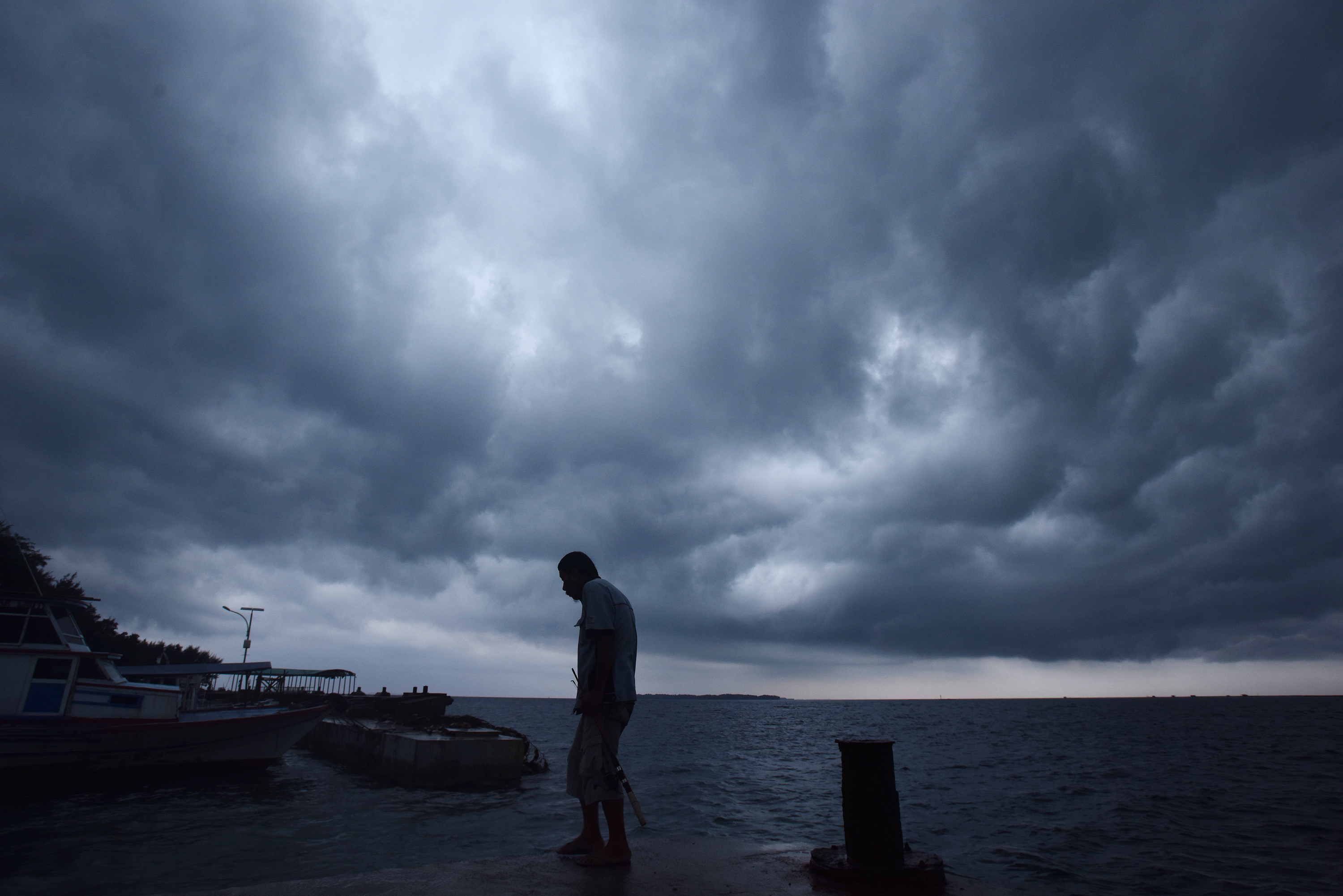 Potret warga beraktivitas di dermaga dengan latar belakang awan gelap.