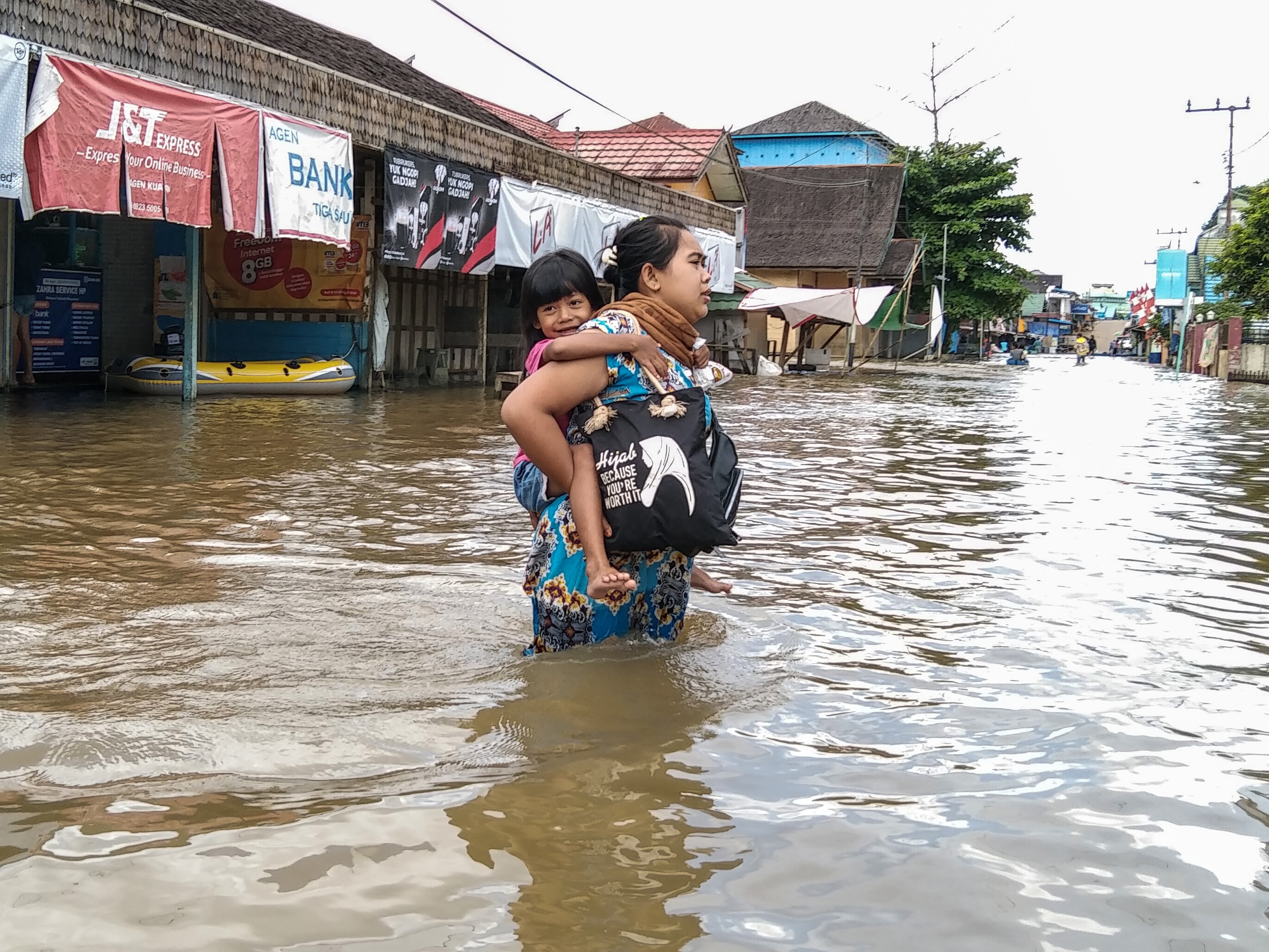 Seorang ibu menggendong anaknya melintasi banjir di permukiman Desa Mentaya Hulu, Kotawaringin Timur, Kalimantan Tengah, Kamis (7/10/2021).