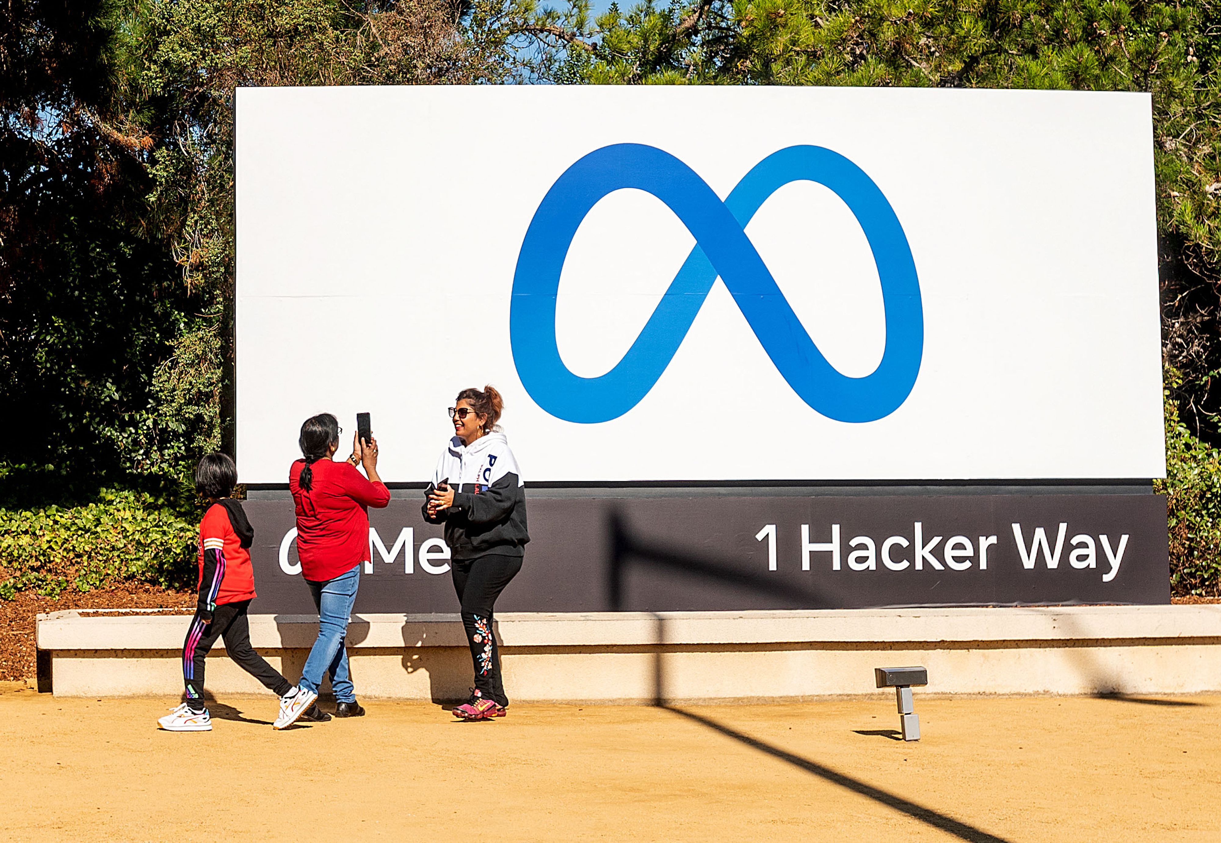 Warga berfoto dengan latar belakang logo Meta, perusahaan induk Facebook, di Menlo Park, California, AS.