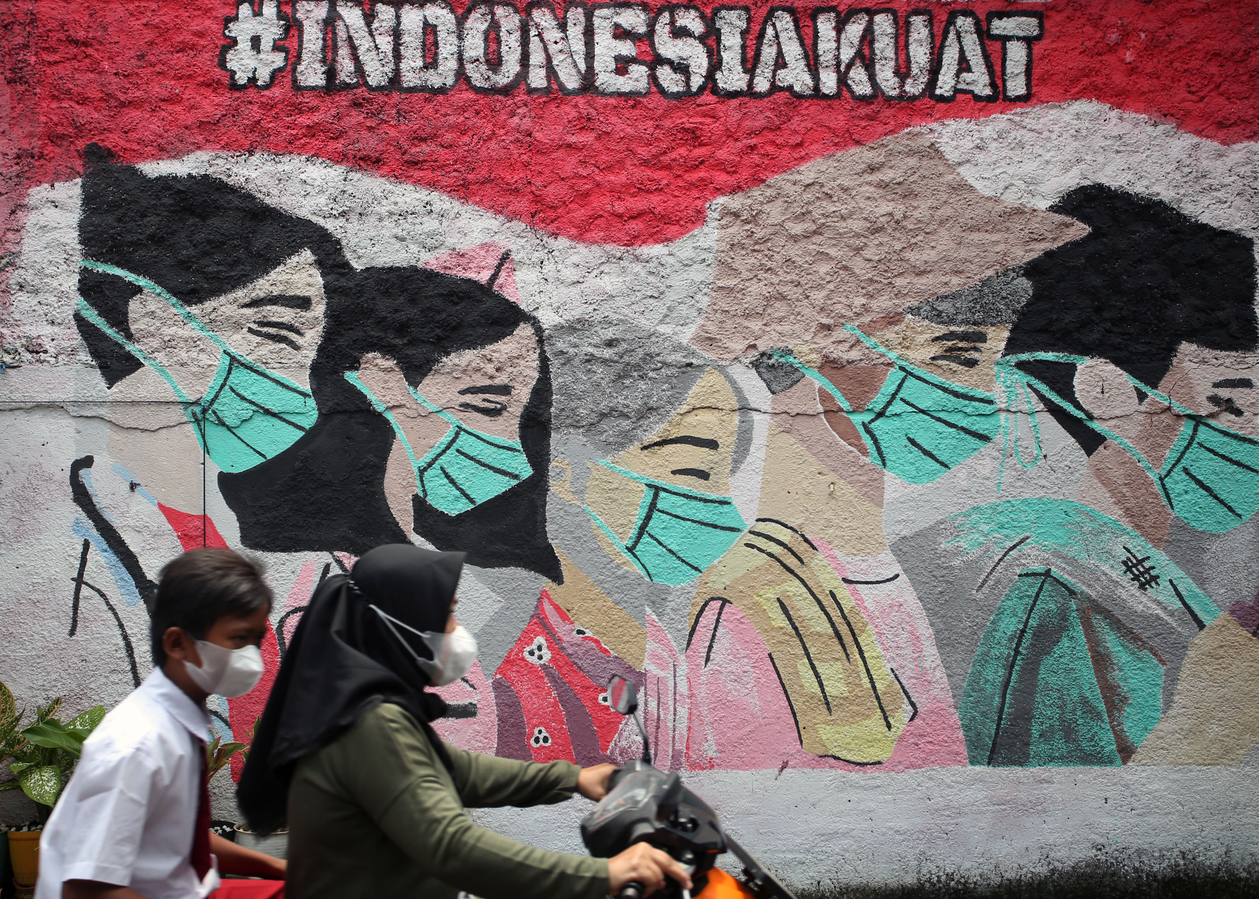 Pengendara motor melintasi mural terkait pandemi covid-19 di wilayah Tangerang Selatan.