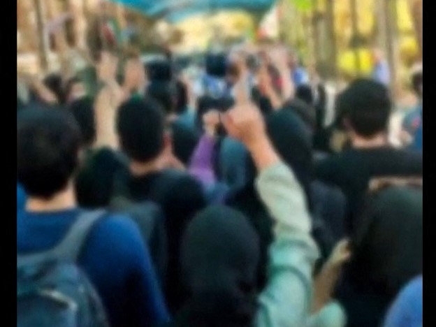 Para mahasiswa meneriakkan slogan-slogan saat mereka mereka mengepalkan tangan mereka selama protes di Universitas Teheran.