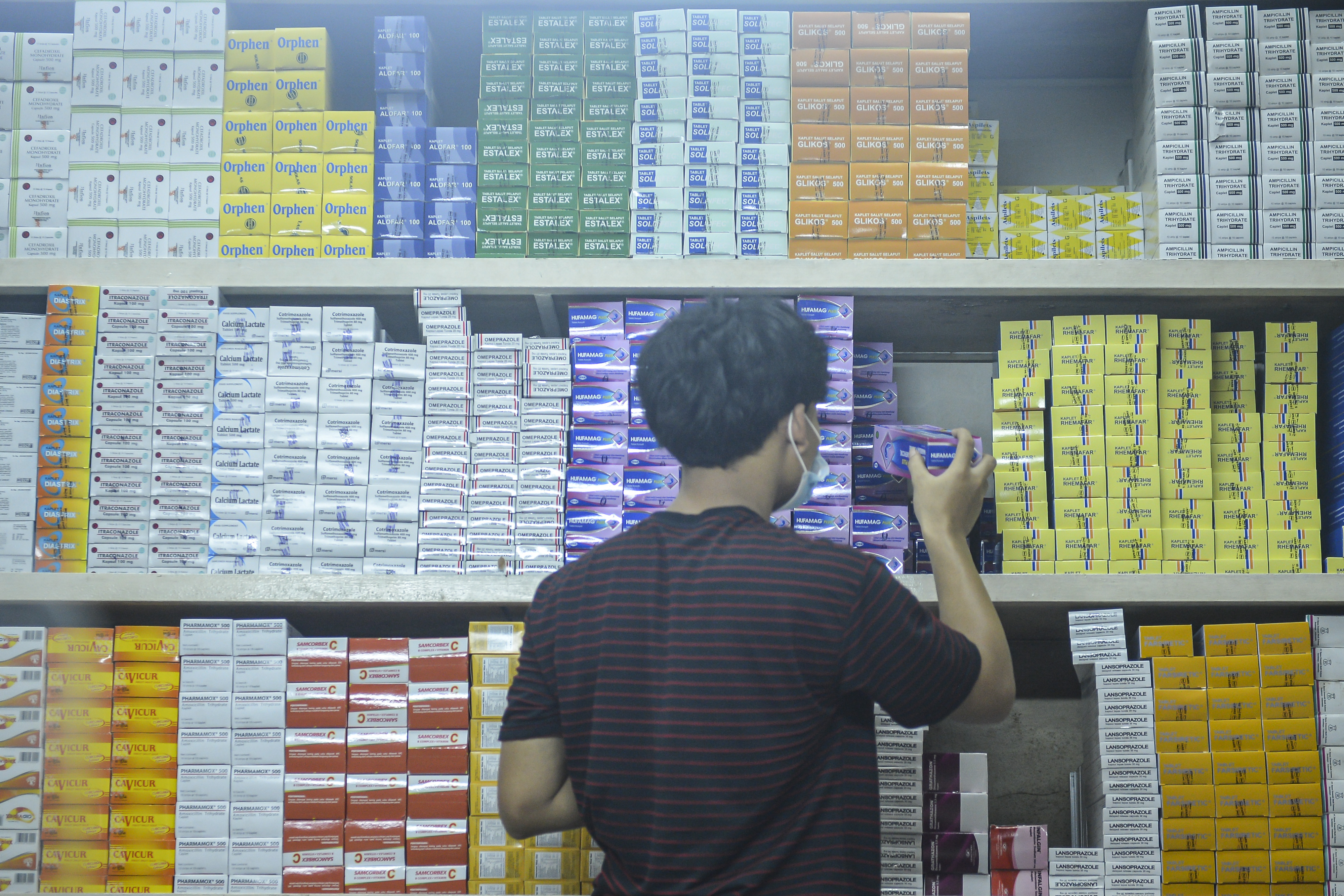 Karyawan toko obat tengah menata barang.