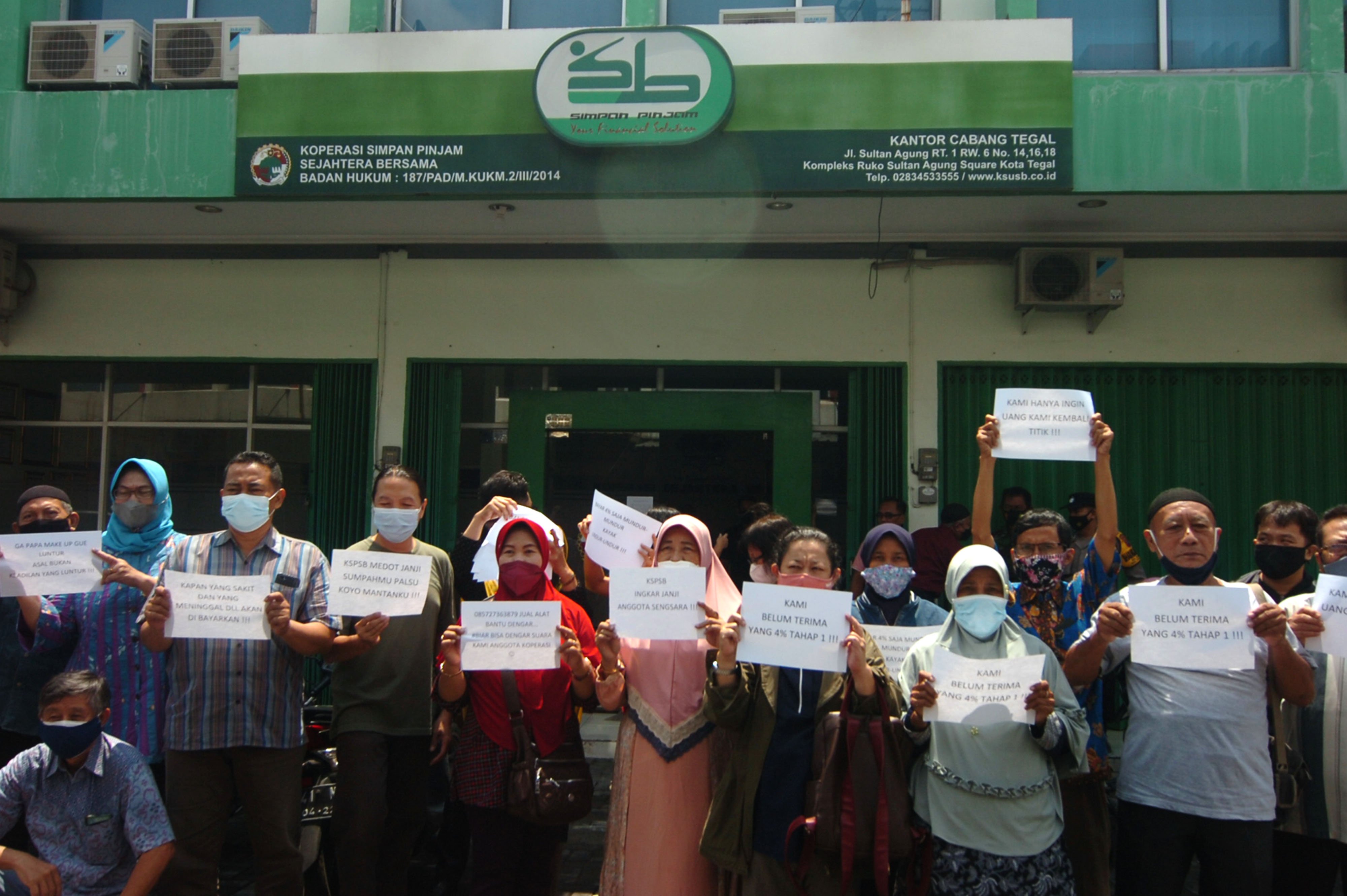 Nasabah koperasi bentangkan tulisan saat mendatangi kantor Koperasi Simpan Pinjam Sejahtera Bersama di Tegal, Jawa Tengah.