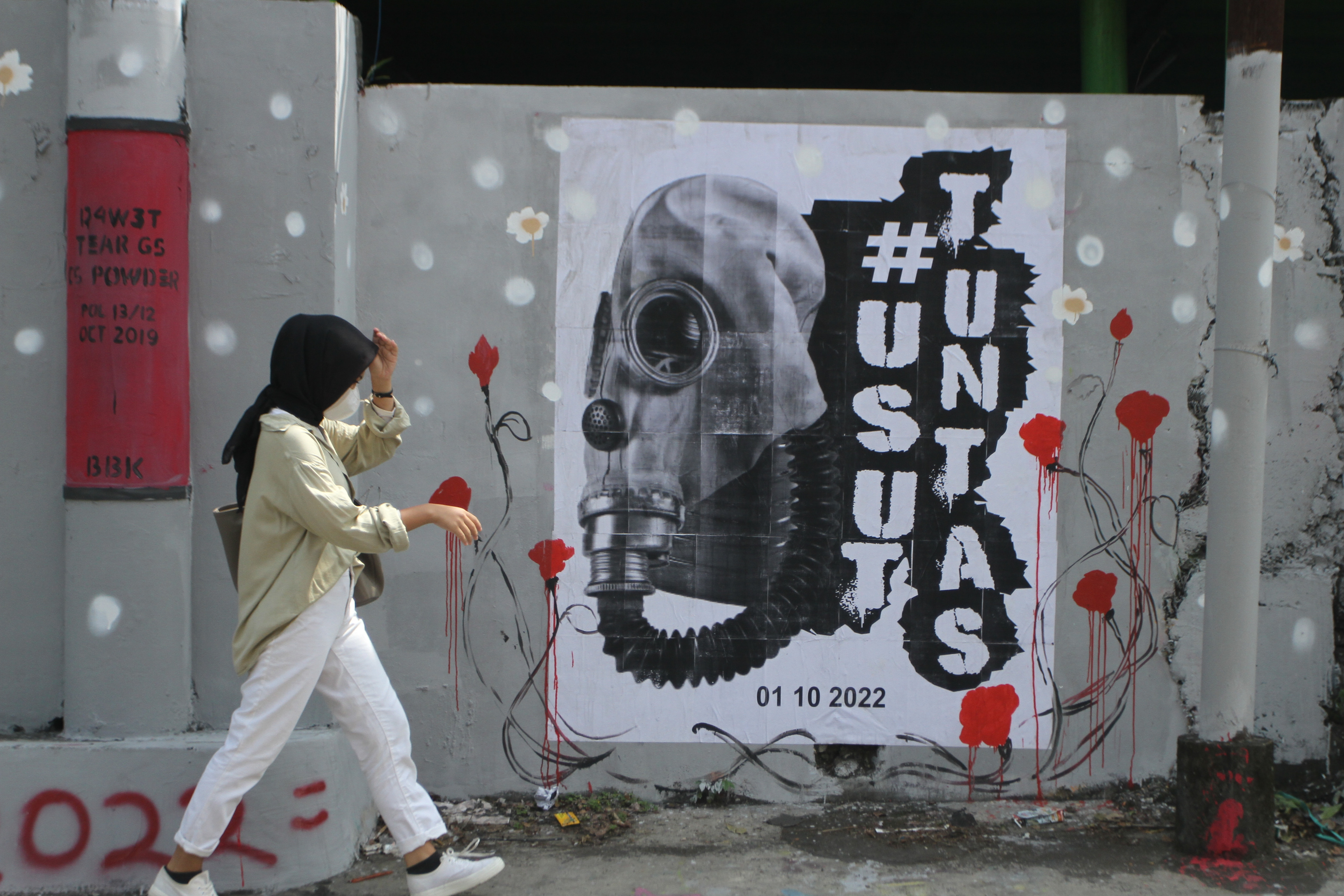 Pejalan kaki melintasi mural bertema tragedi Kanjuruhan di Jalan Simpang Gajayana, Malang, Jawa Timur.