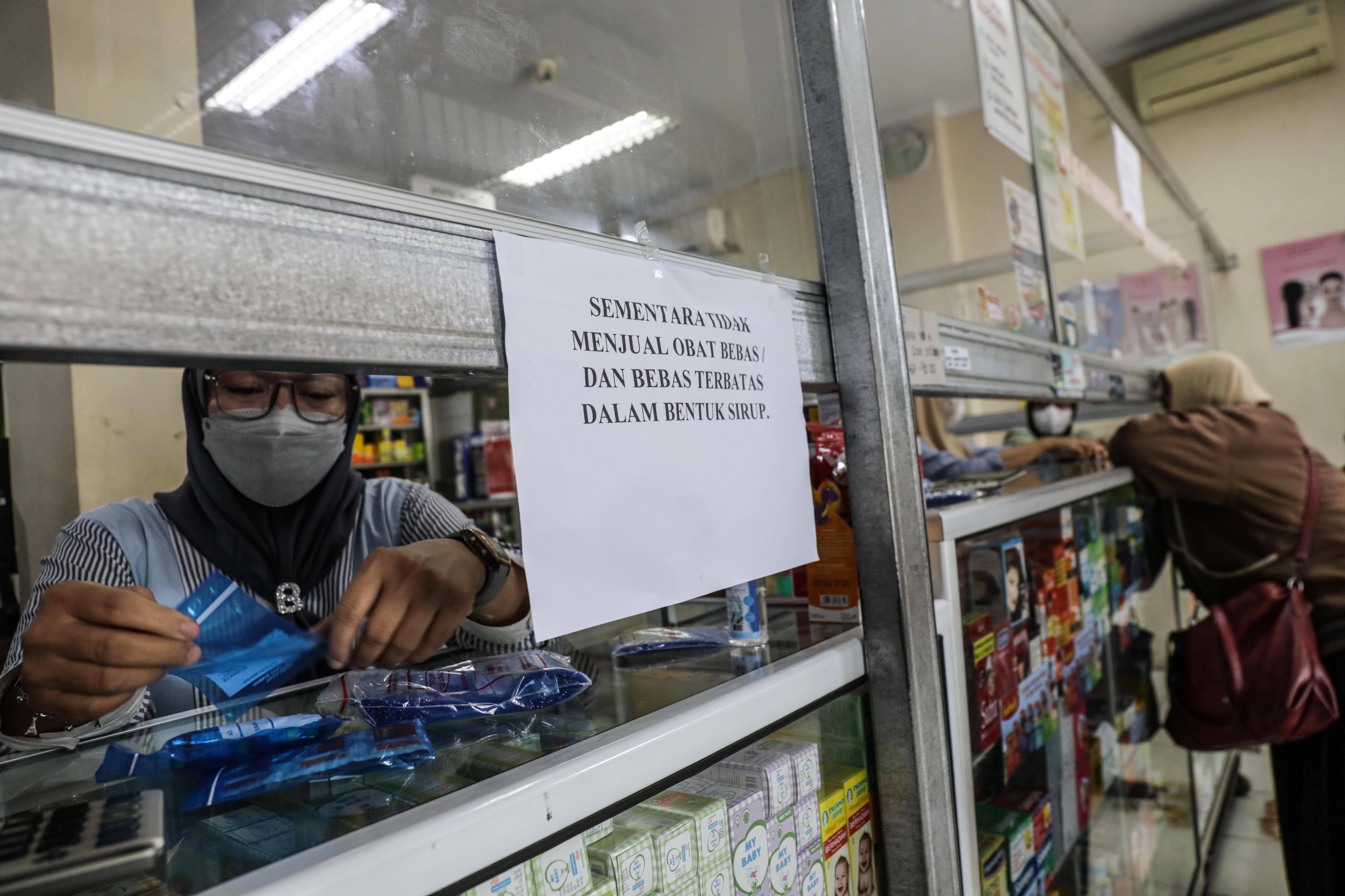 Petugas apotek menyiapkan obat di dekat tulisan penghentian sementara penjualan obat sirop.