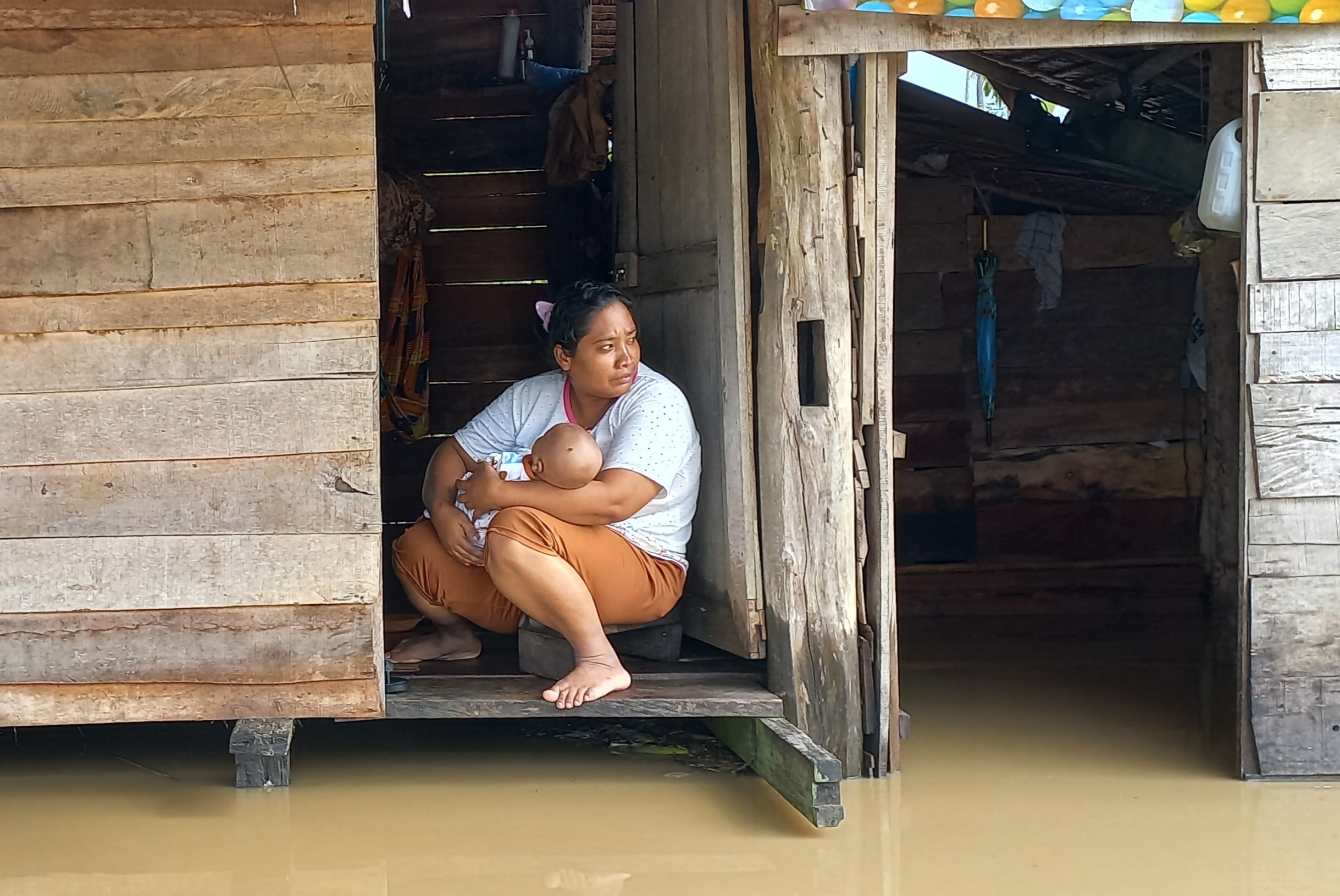 Seorang ibu menggendong anaknya mengharapkan bantuan datang dari banjir yang melanda Kabupaten Aceh Timur, Aceh, Jumat (7/10).