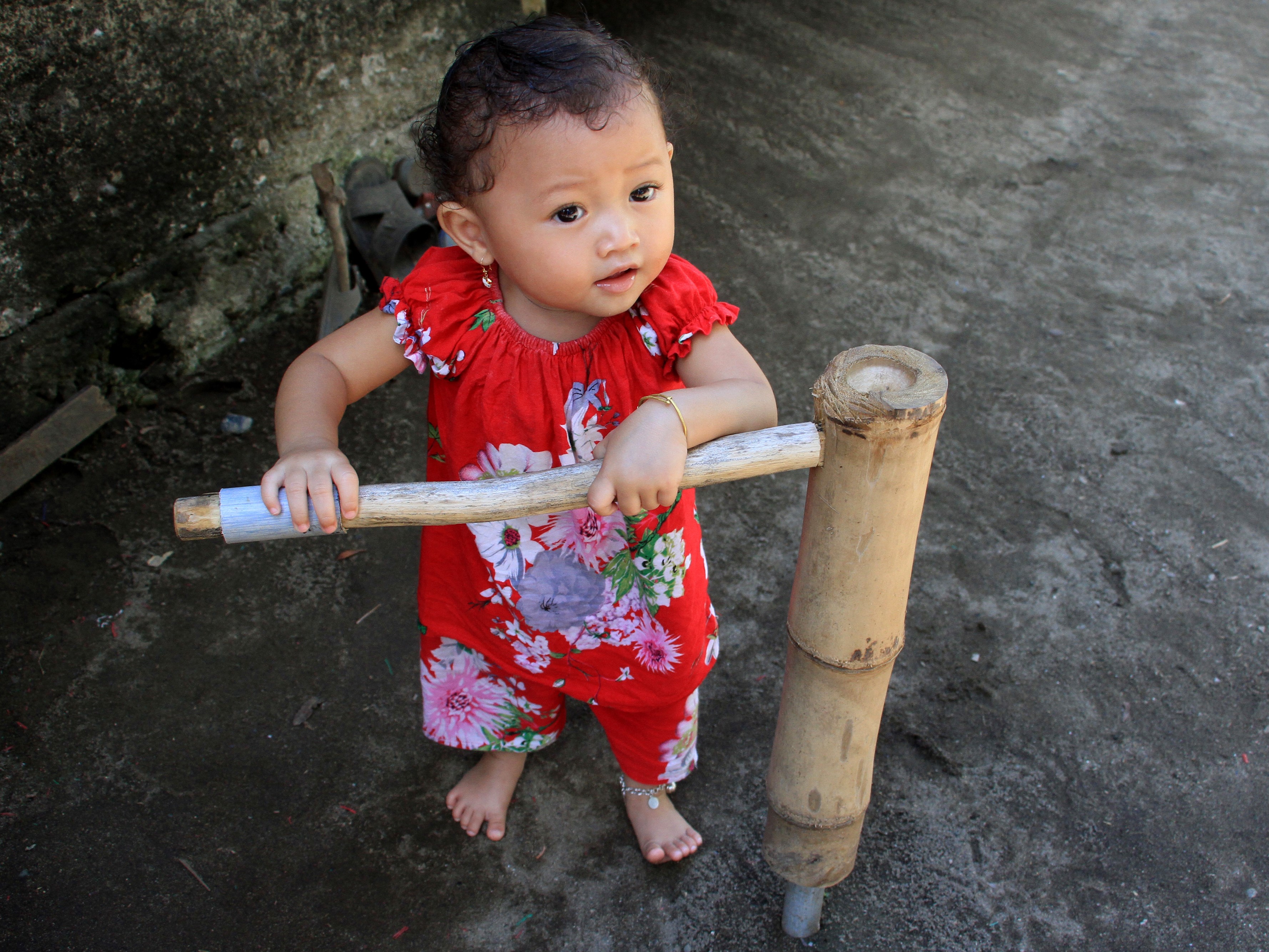 Seorang anak belajar berjalan dengan menggunakan alat bantu jalan anak tradisional atau weng tradisional yang terbuat dari bambu.