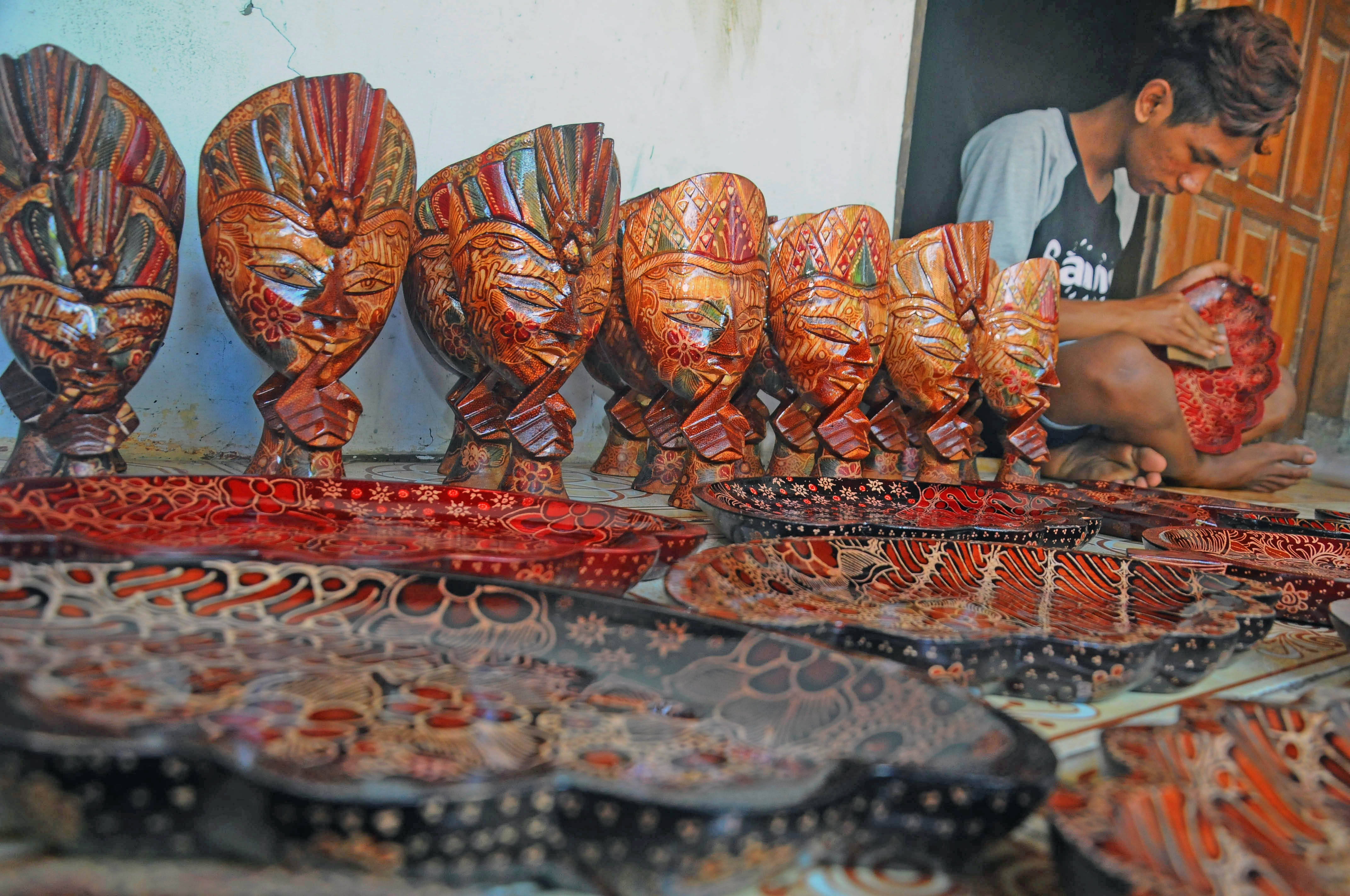 Seorang perajin menghaluskan kerajinan kayu batik.