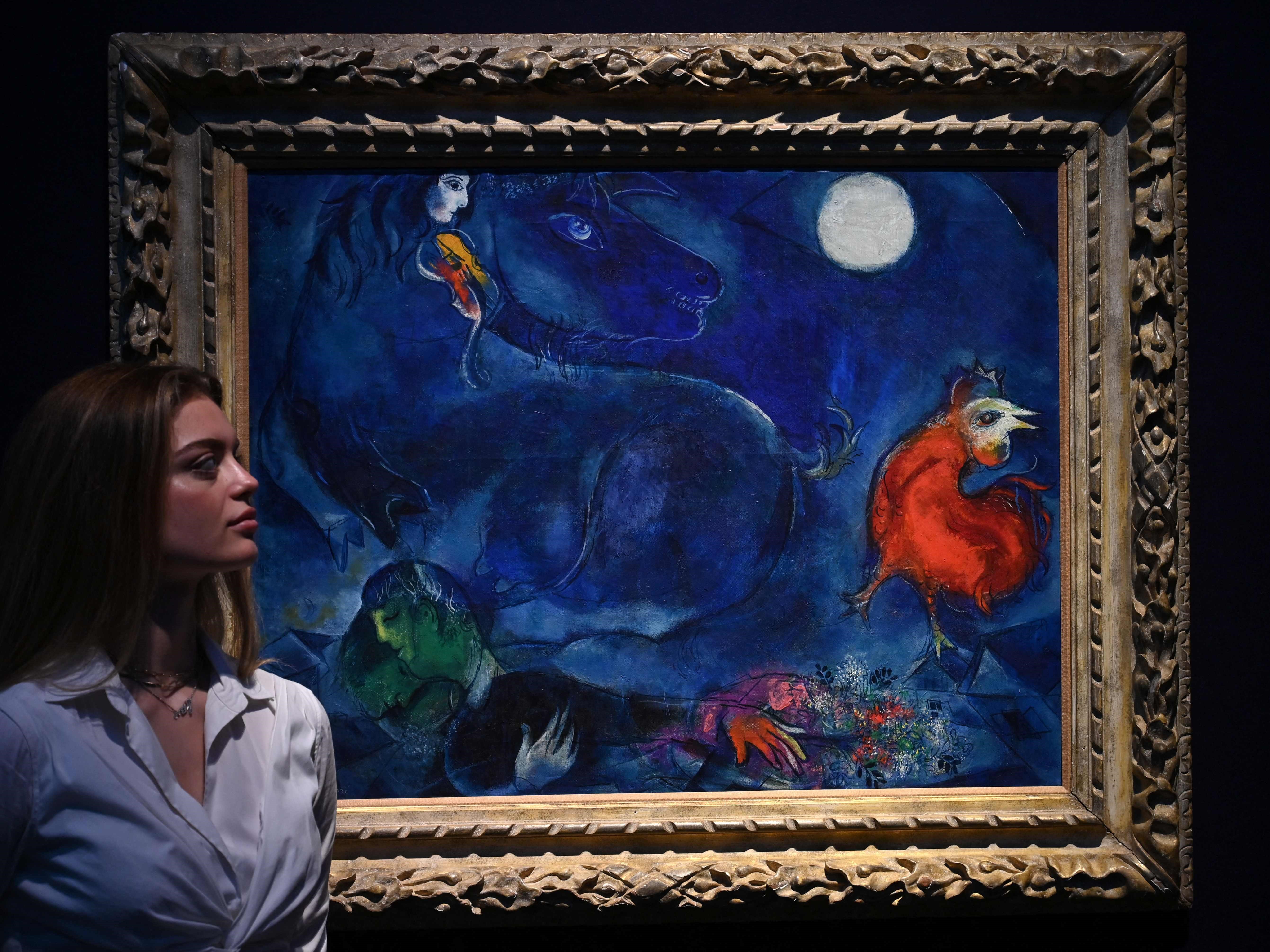 Seorang asisten galeri berpose di sebelah karya seni berjudul Le Cheval Bleu (Kuda Biru) karya pelukis Prancis Marc Chagall.