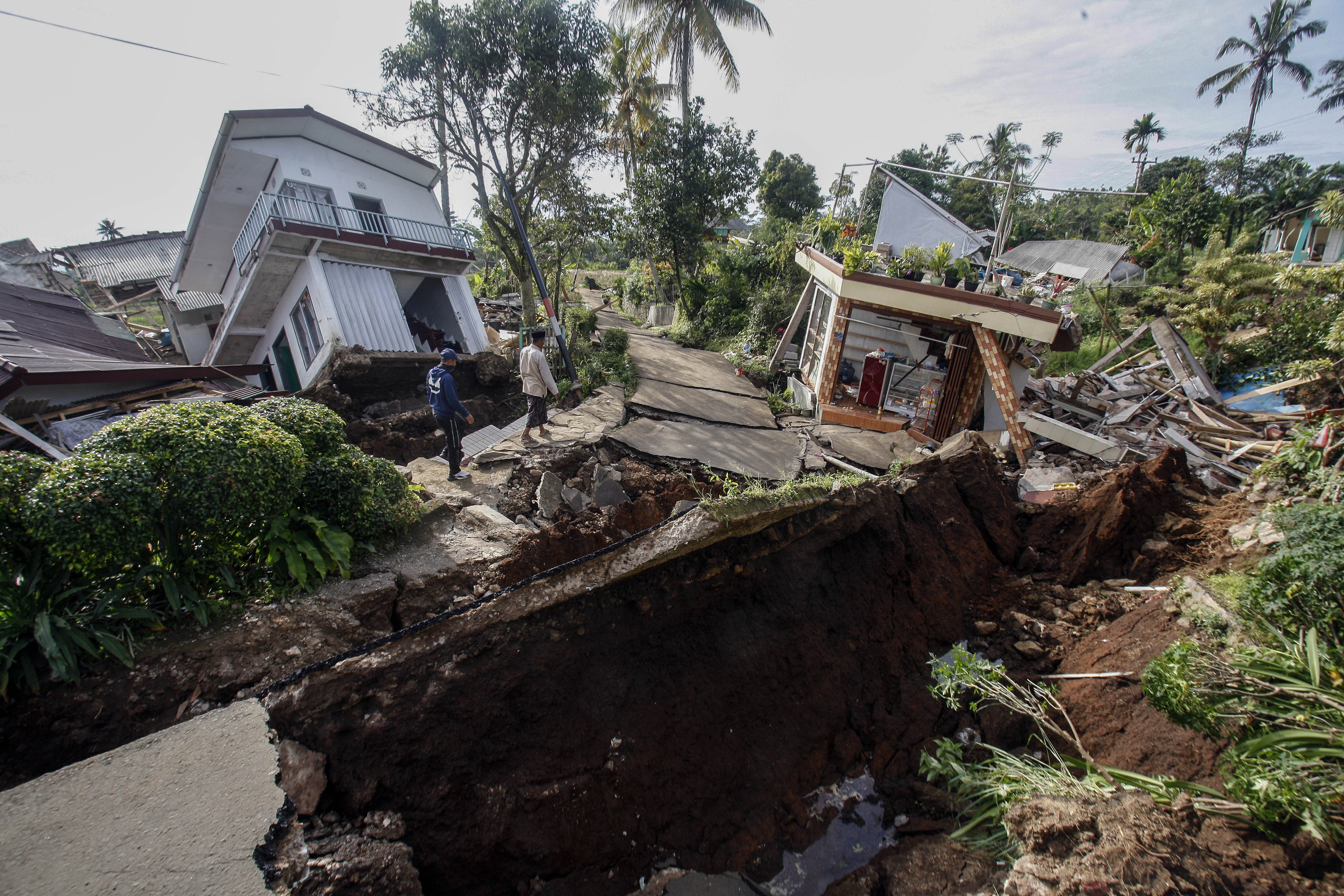 Warga melintas di dekat reruntuhan bangunan akibat gempa di Kabupaten Cianjur, Jawa Barat.