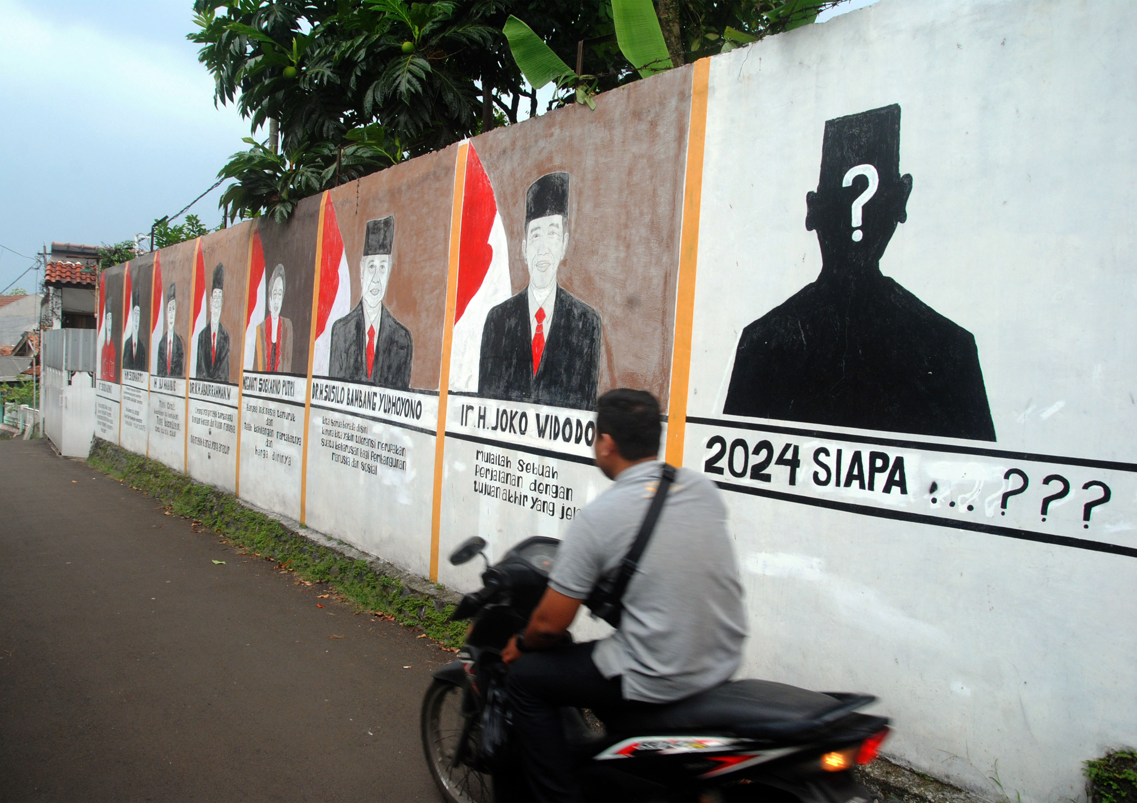 Pengendara motor melintasi mural terkait pemilihan presiden.