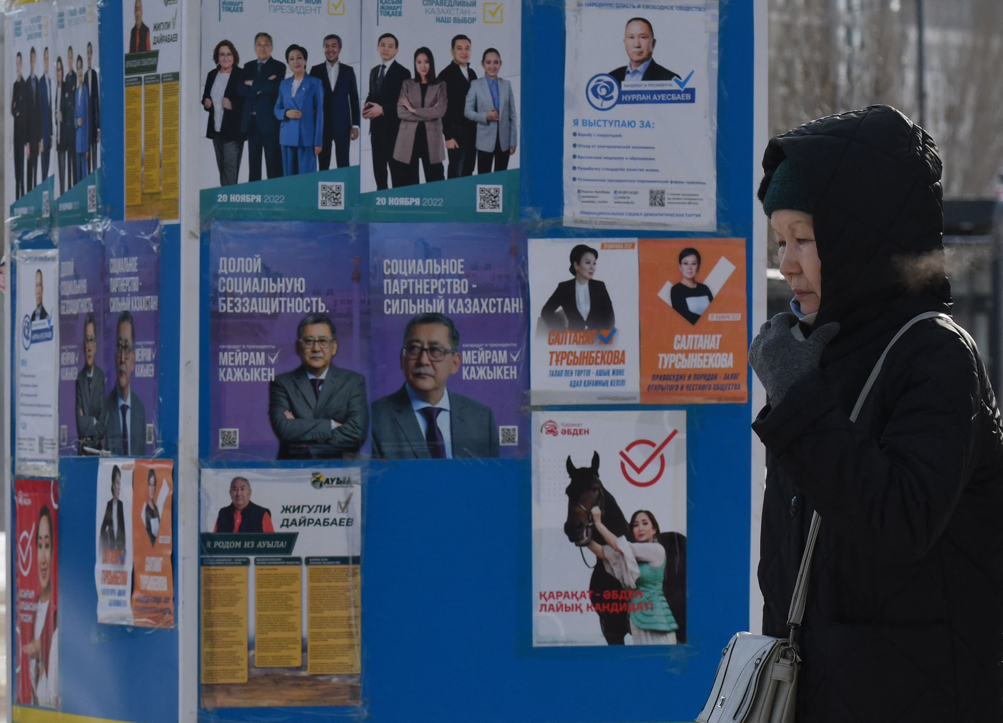 Warga melintas di depan tembok yang ditempeli poster kandidat presiden Kazakhstan di Astana.