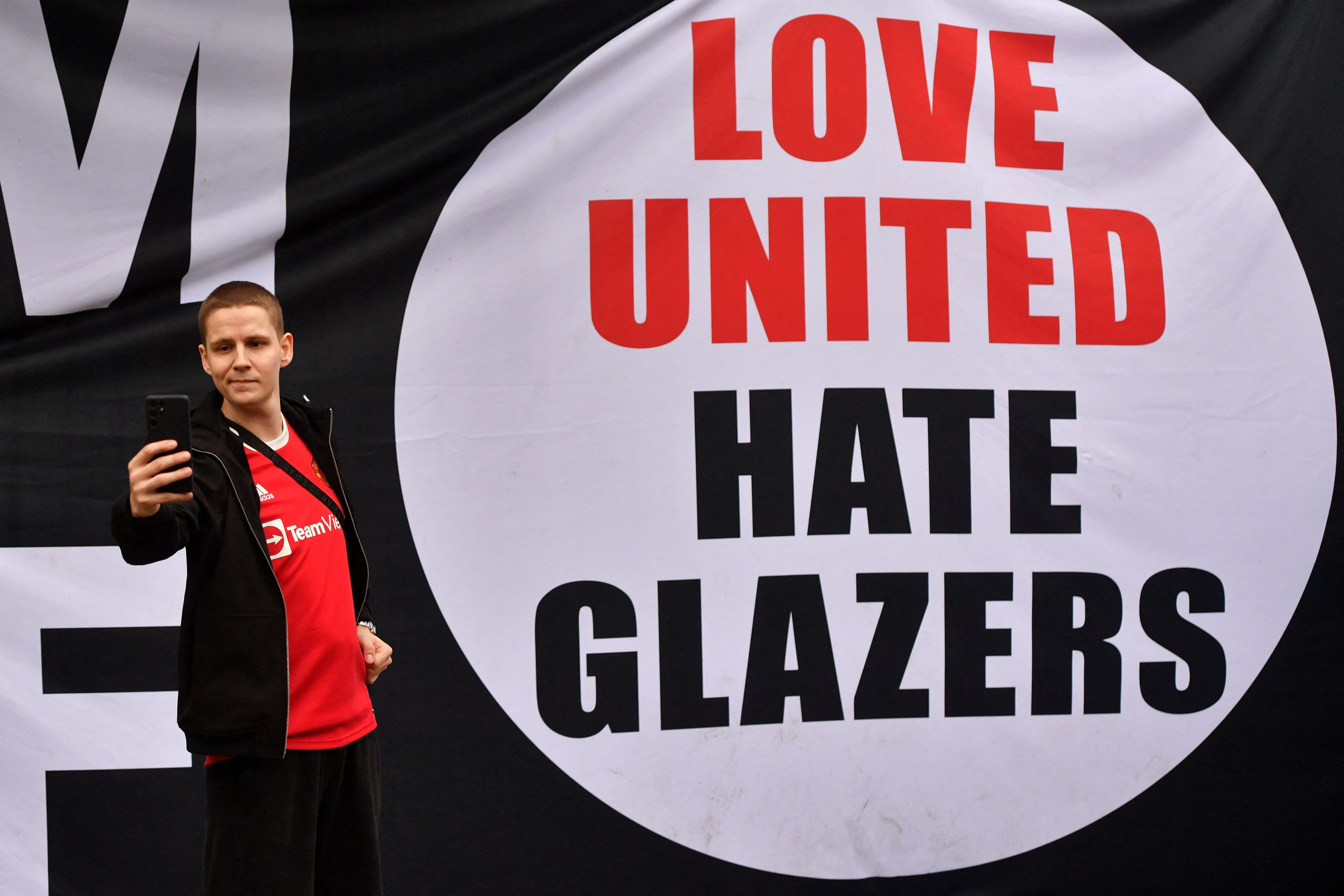 Seorang pendukung Manchester United berswafoto di depan spanduk bertuliskan, 'Love United, Hate Glazers' di luar Old Trafford.