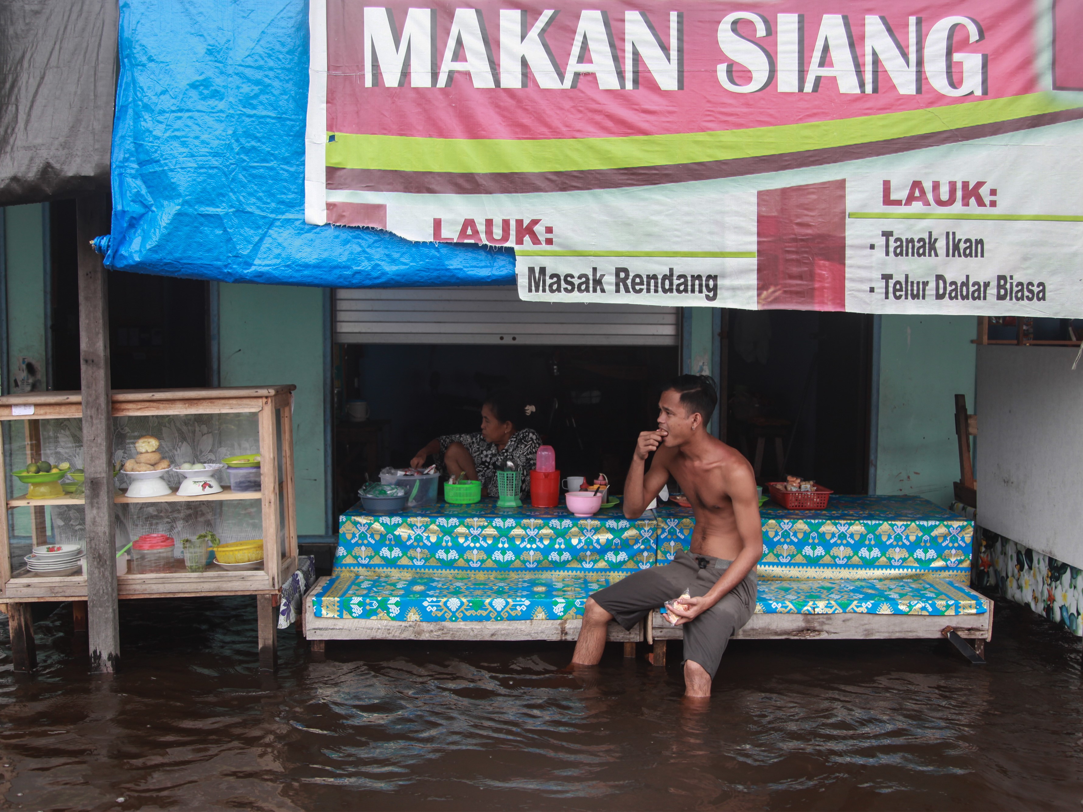 Warga duduk di depan warung makan yang terendam banjir di Jalan Mendawai Induk, Palangka Raya, Kalimantan Tengah, Kamis (17/11/2022).