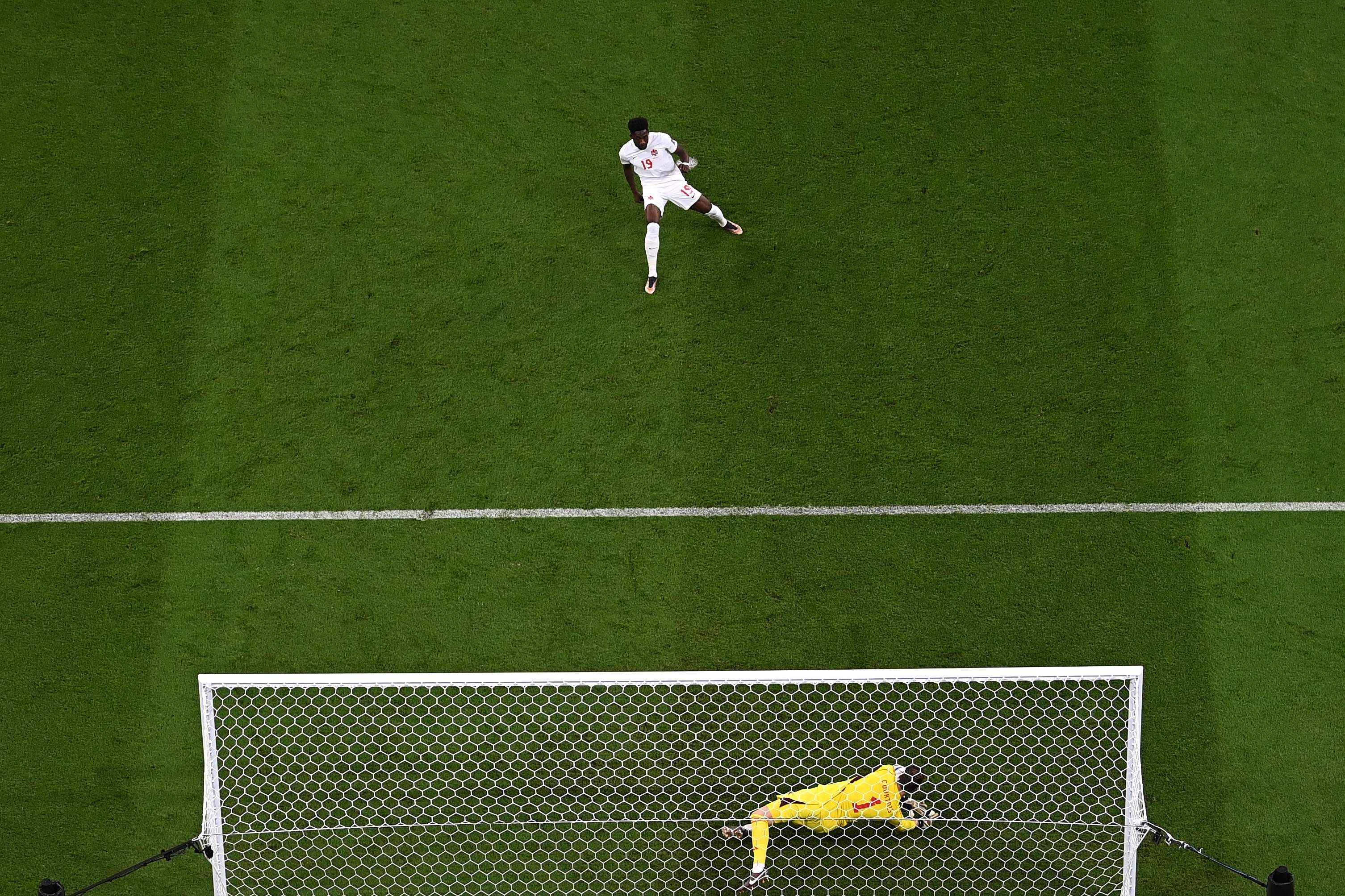 Penjaga gawang Belgia Thibaut Courtois (bawah) menahan eksekusi penalti pemain Kanada Alphonso Davies