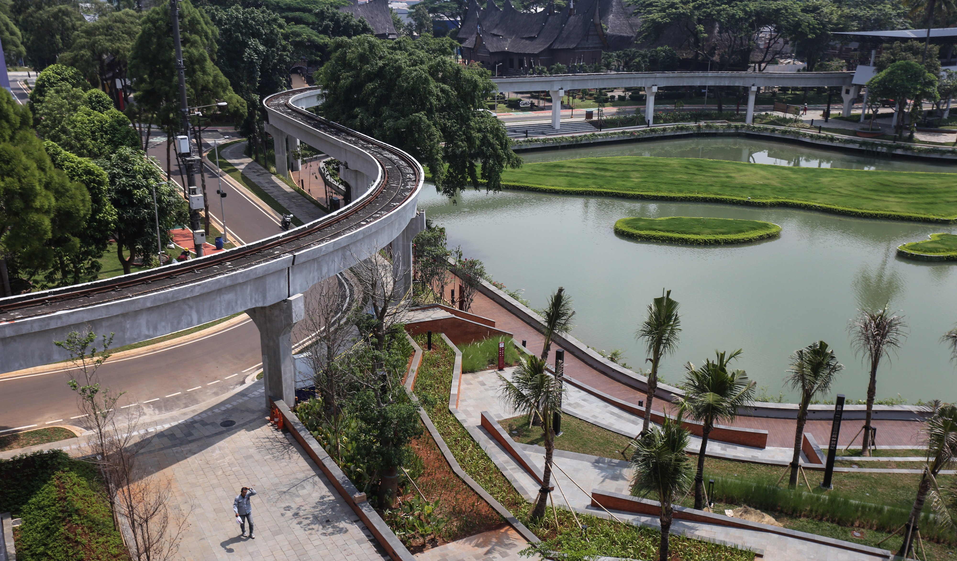 Pekerja berjalan di area danau kawasan TMII, Jakarta.