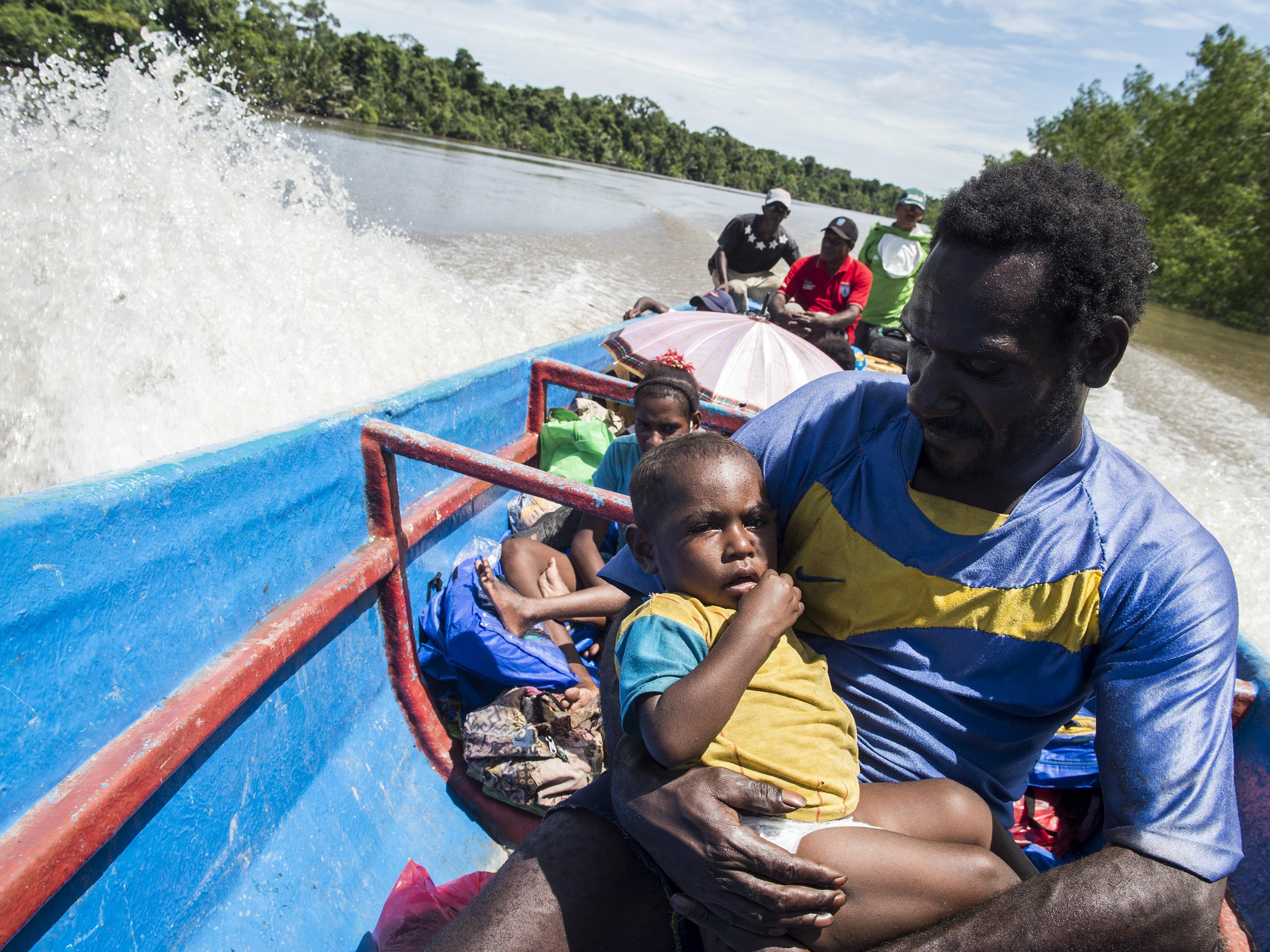 Orangtua menggendong anaknya saat berada di kapal longboat menuju Distrik Jetsy di Kabupaten Asmat, Papua.