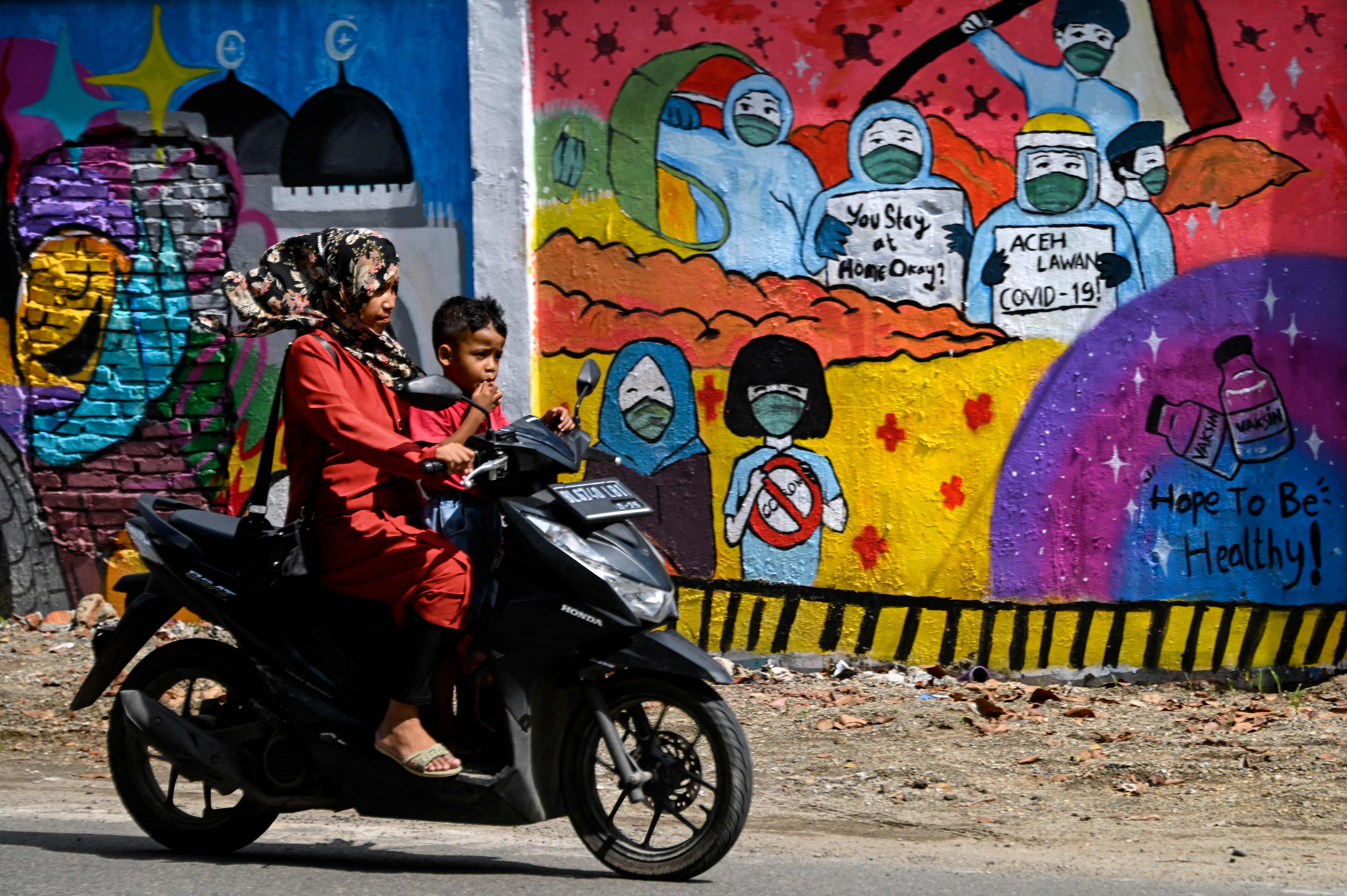 Warga tanpa masker mengendarai motor melewati mural tantang covid-19