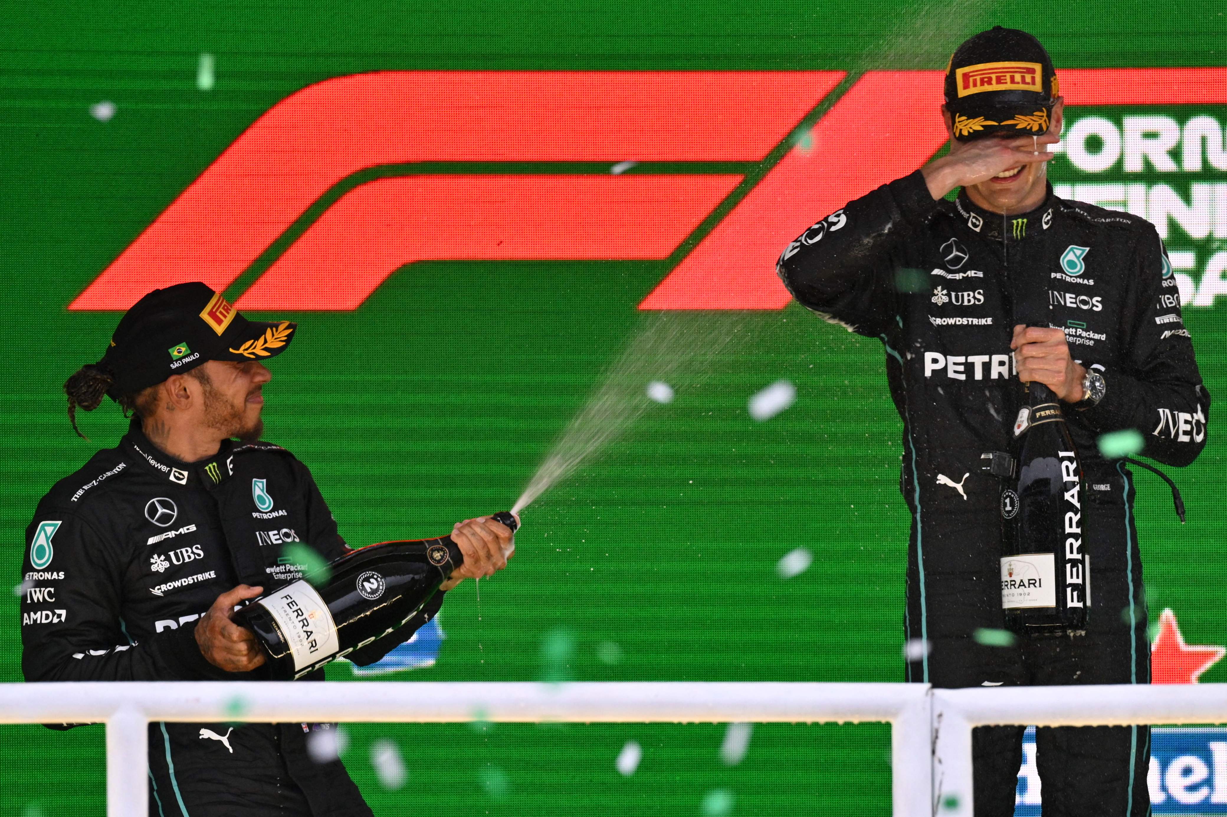 Pembalap Mercedes Lewis Hamilton (kiri) menyiram rekan setimnya George Russell di podium usai finis 1-2 di GP Brasil.