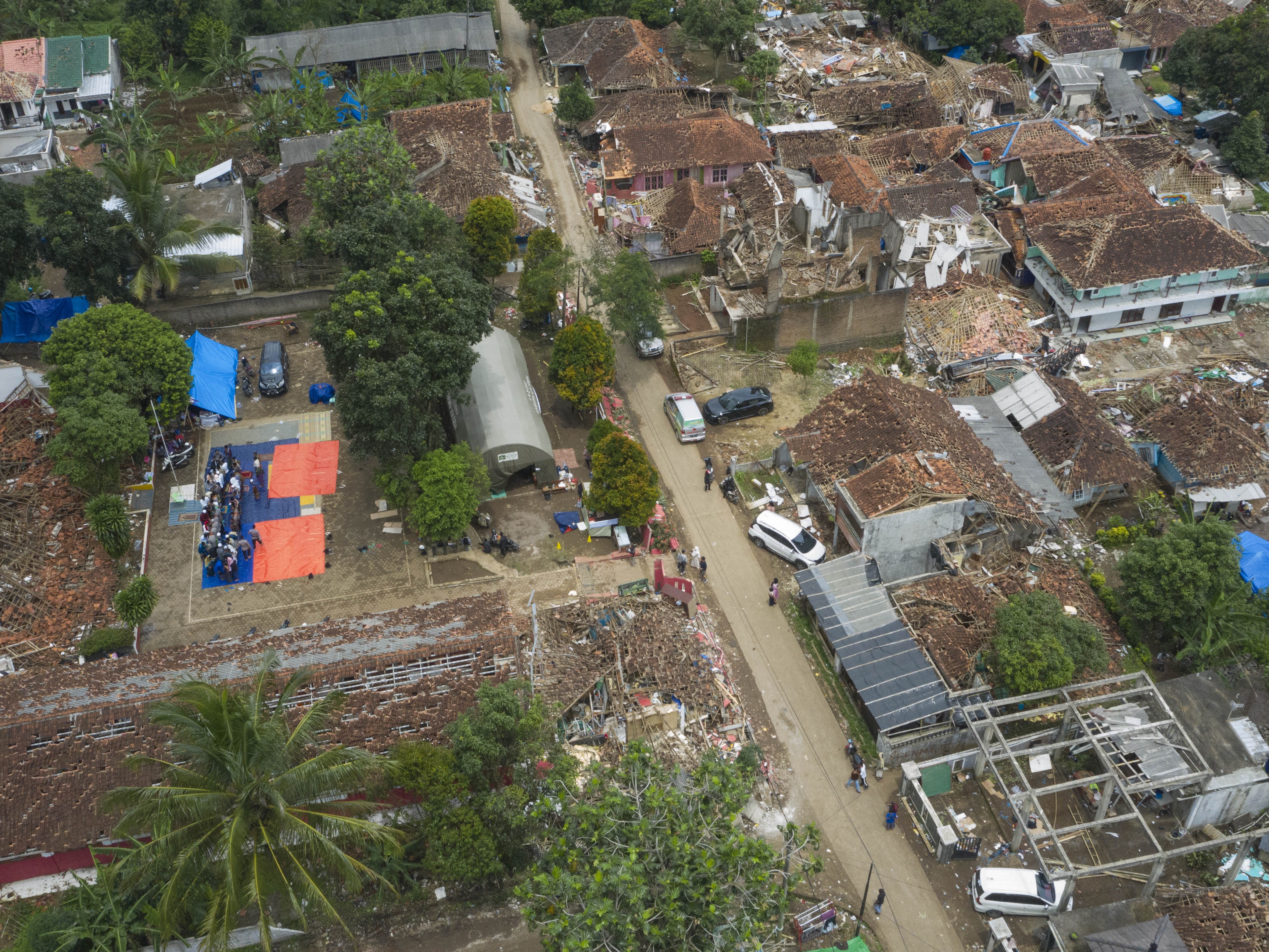 Foto udara jemaah berjabat tangan usai mengikuti shalat Jumat di antara reruntuhan bangunan pascagempa bumi Cianjur di Garogol Kidul.