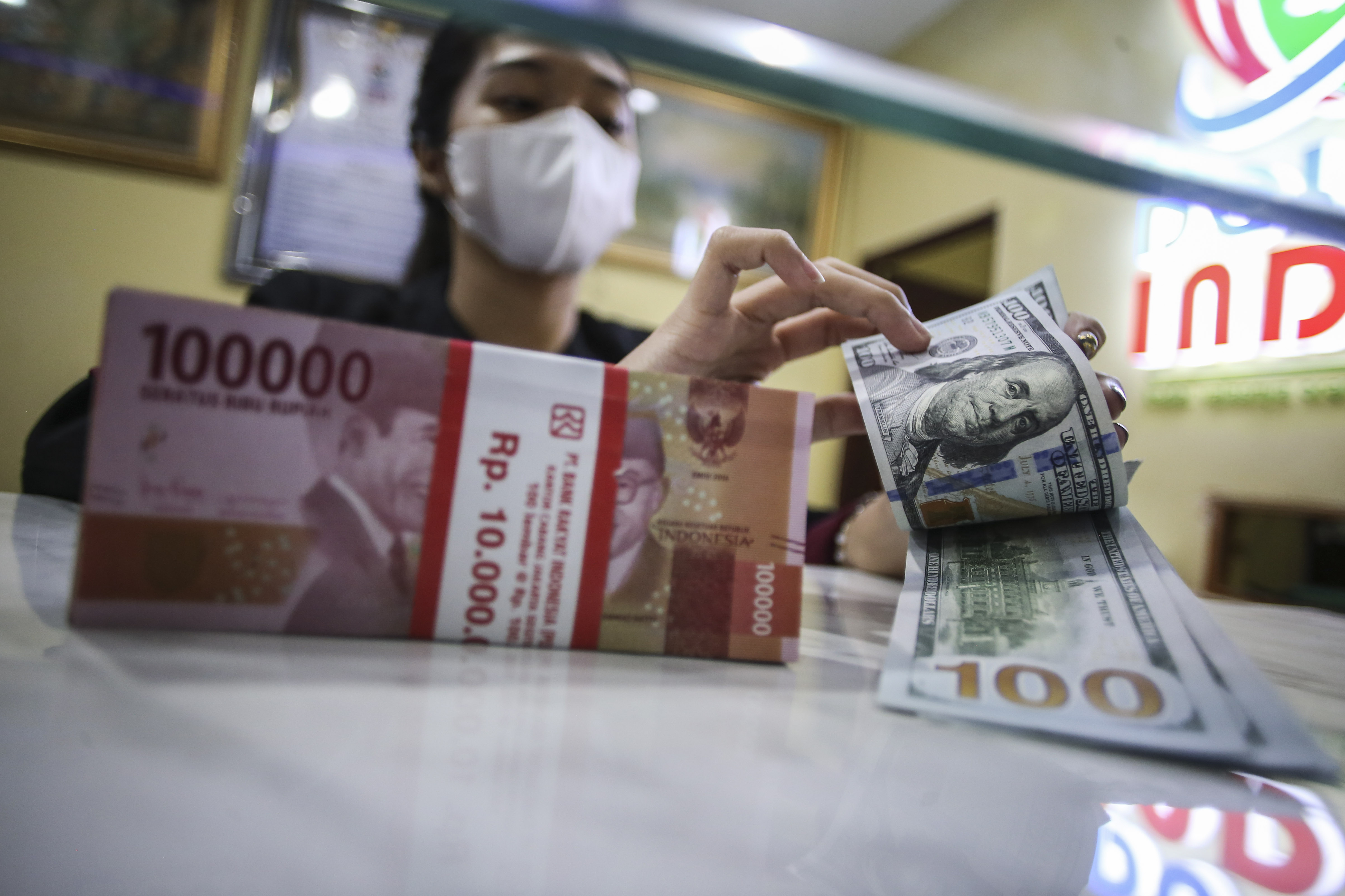 Petugas di gerai penukaran valas menghitung pecahan dolar AS.