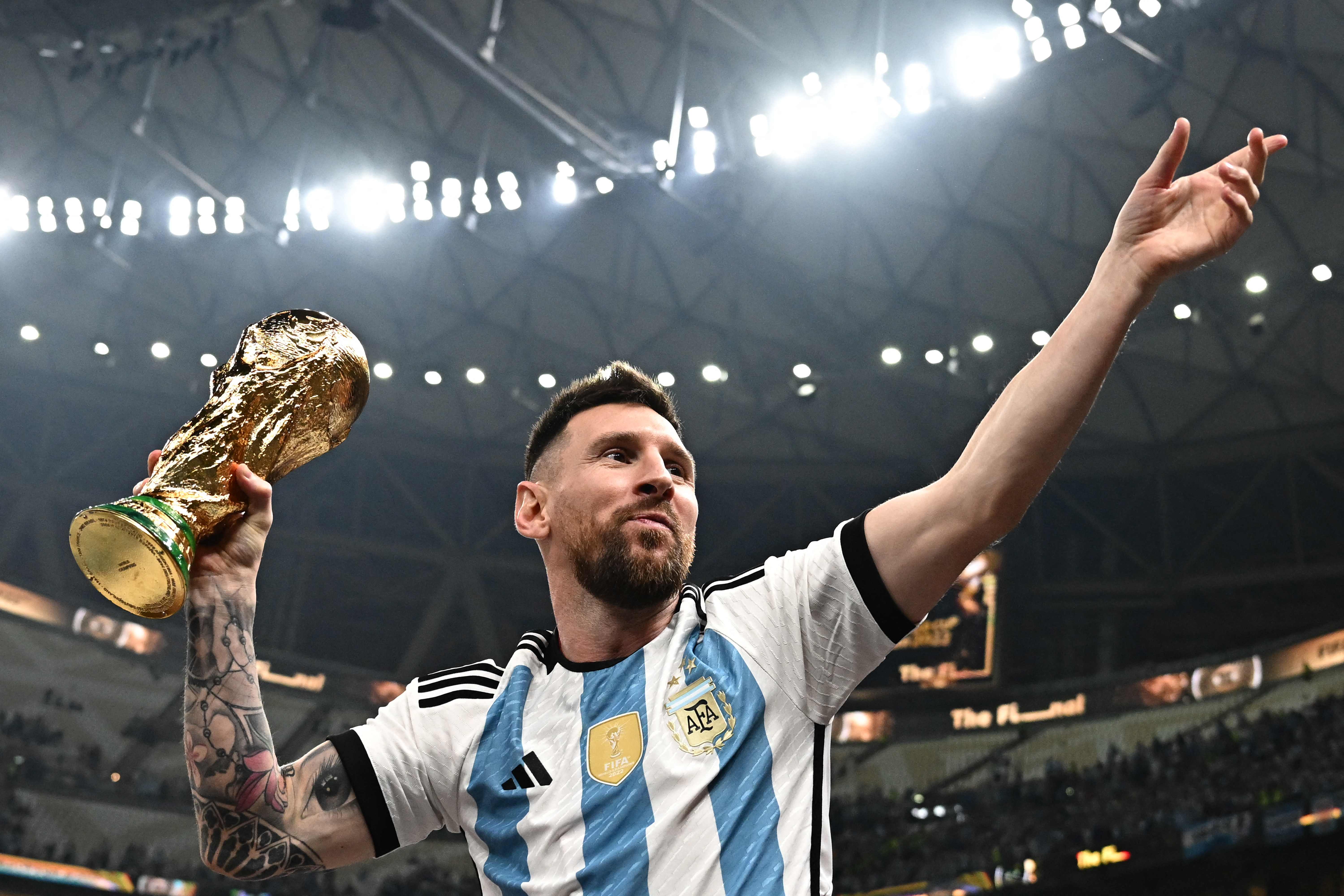 Kapten timnas Argentina Lionel Messi mengangkat trofi Piala Dunia yang dimenanginya setelah mengalahkan Prancis di final, Minggu (18/12).