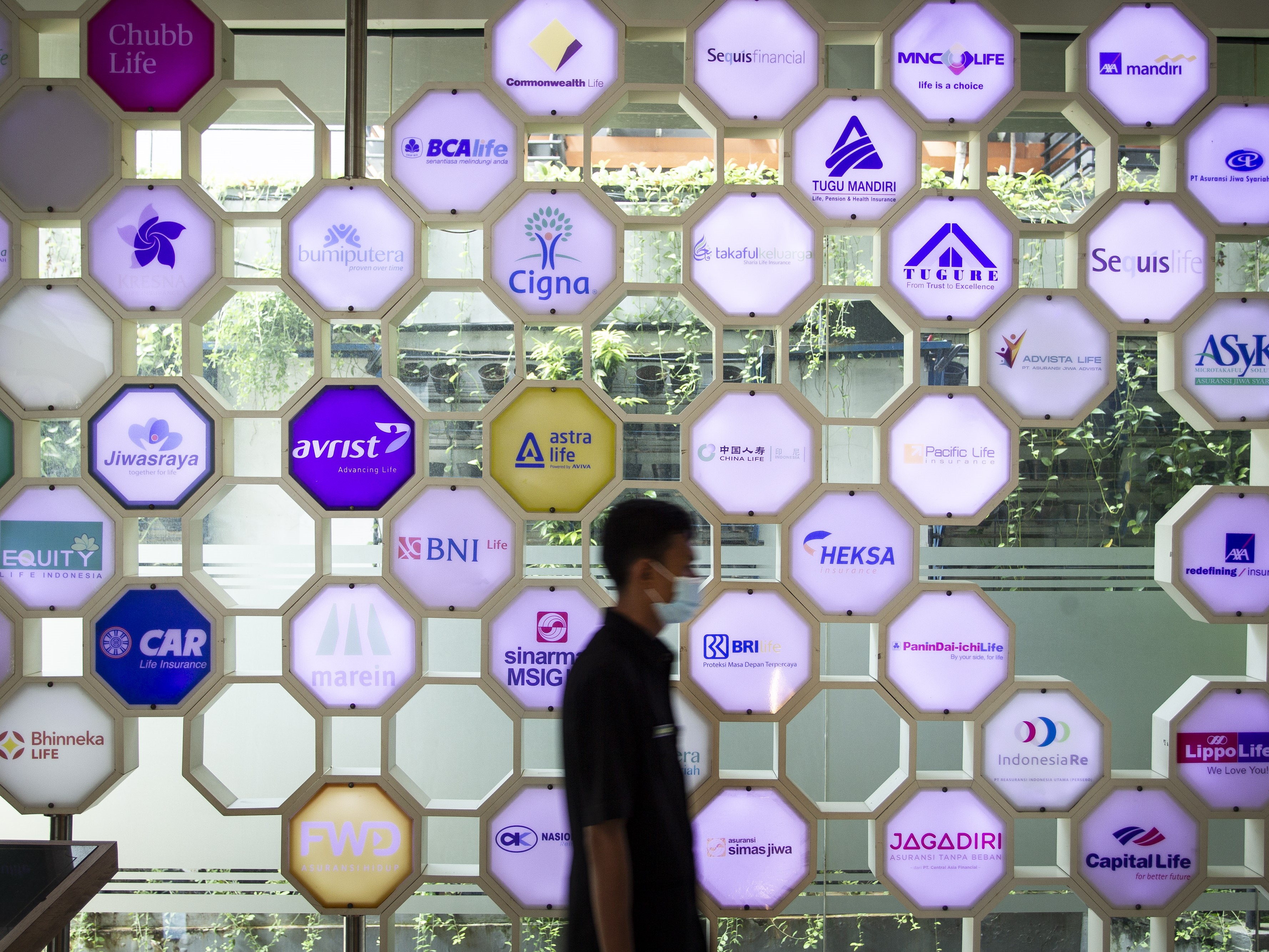 Petugas keamanan berjalan di depan berbagai logo perusahaan asuransi di kantor Asosiasi Asuransi Jiwa Indonesia (AAJI), Jakarta.