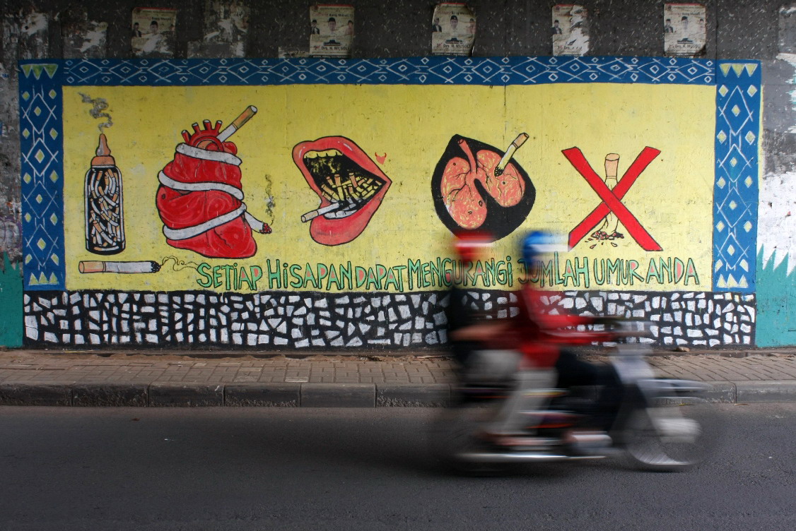 Pengendara melintas digrafiti bahaya merokok bagi kesehatan manusia.