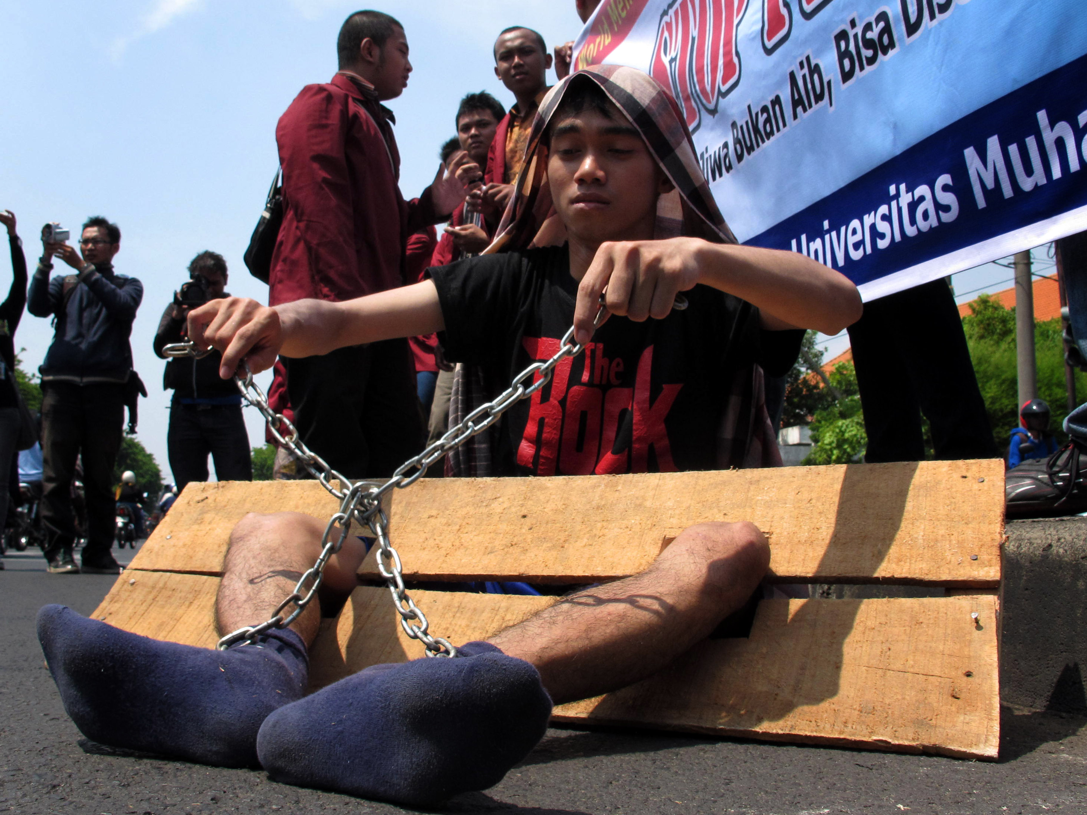 Seorang pengunjuk rasa dari Universitas Muhammadiyah Surabaya, memerankan penderita sakit jiwa yang dipasung.