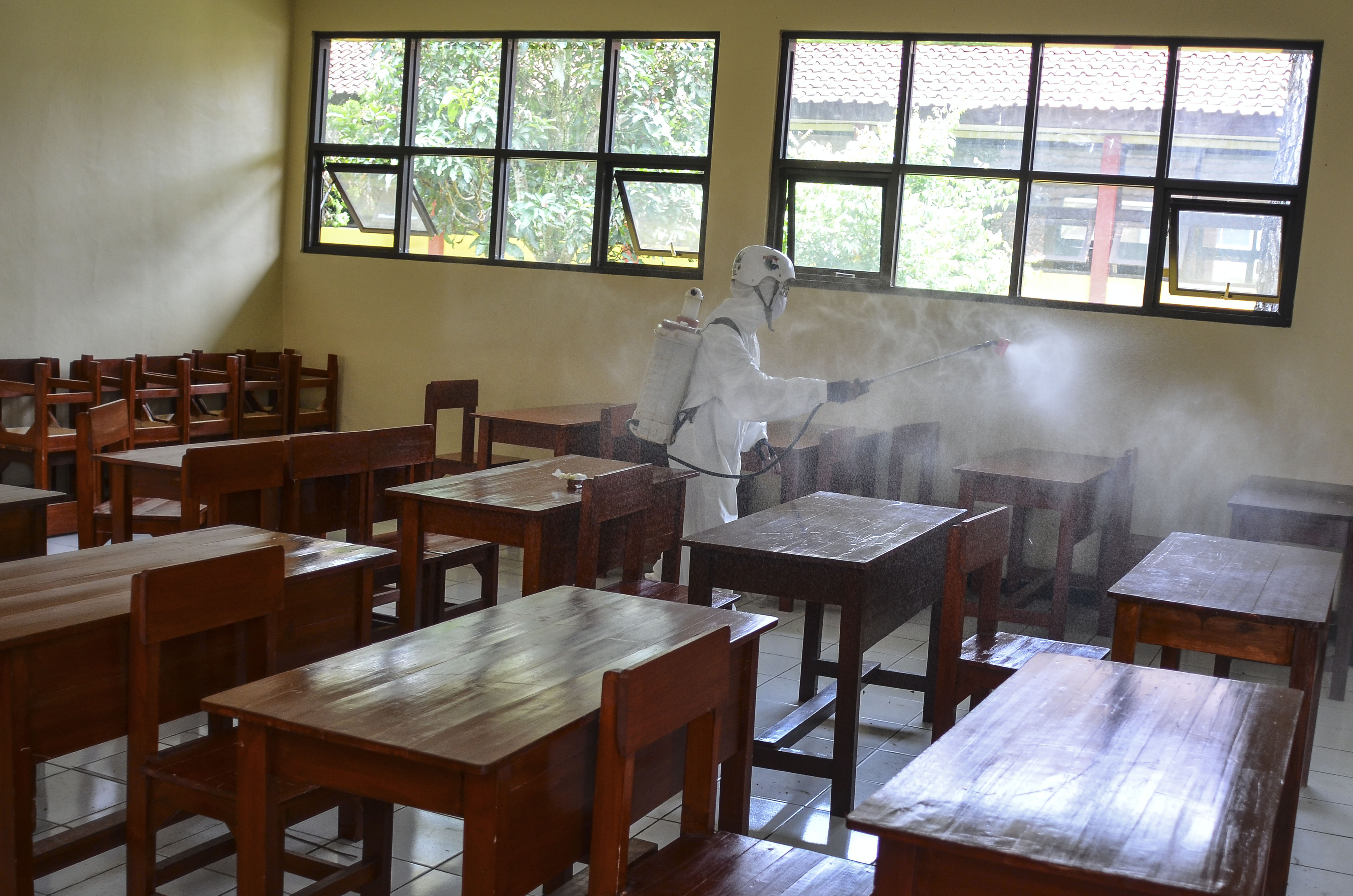 Potret petugas menyemprotkan cairan disinfektan di ruang kelas sekolah.