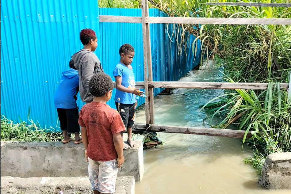 Anak-anak setempat menyaksikan aliran banjir.