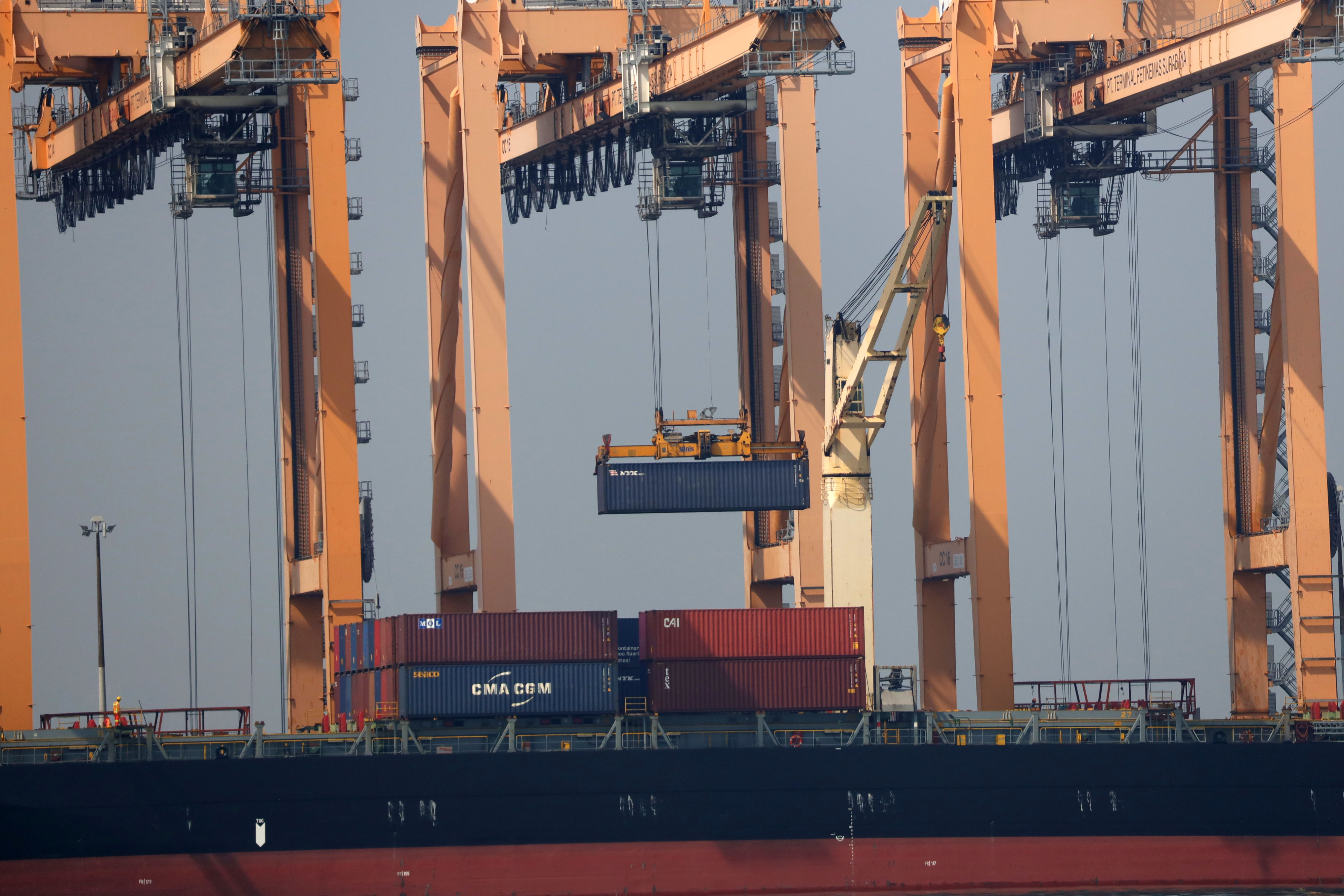 Pekerja membongkar muat kontainer di Terminal Petikemas, Surabaya.