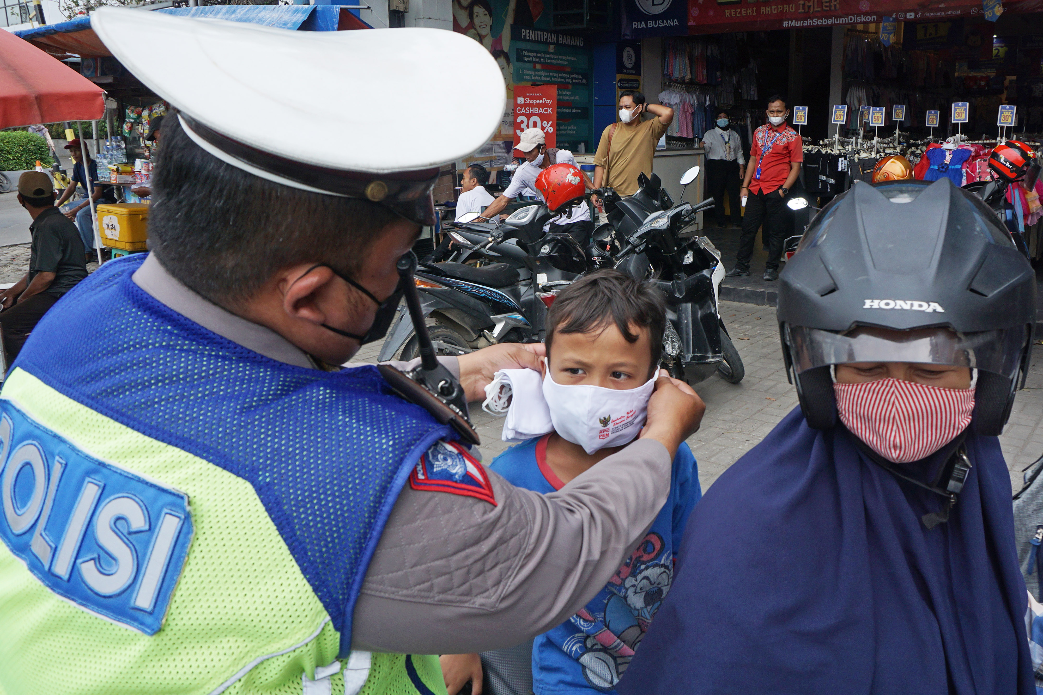 Petugas kepolisian memakaikan masker kepada seorang anak.